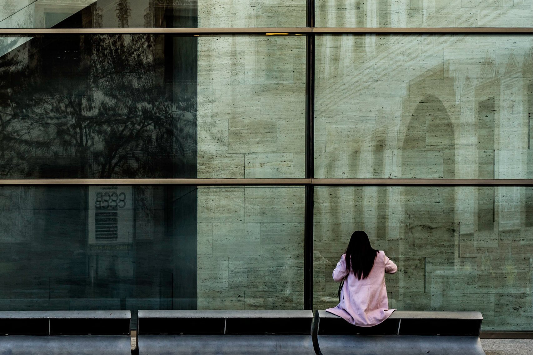 Woman in a pink coat against a reflected glass facade, street photography in Barcelona – bCLPhoto