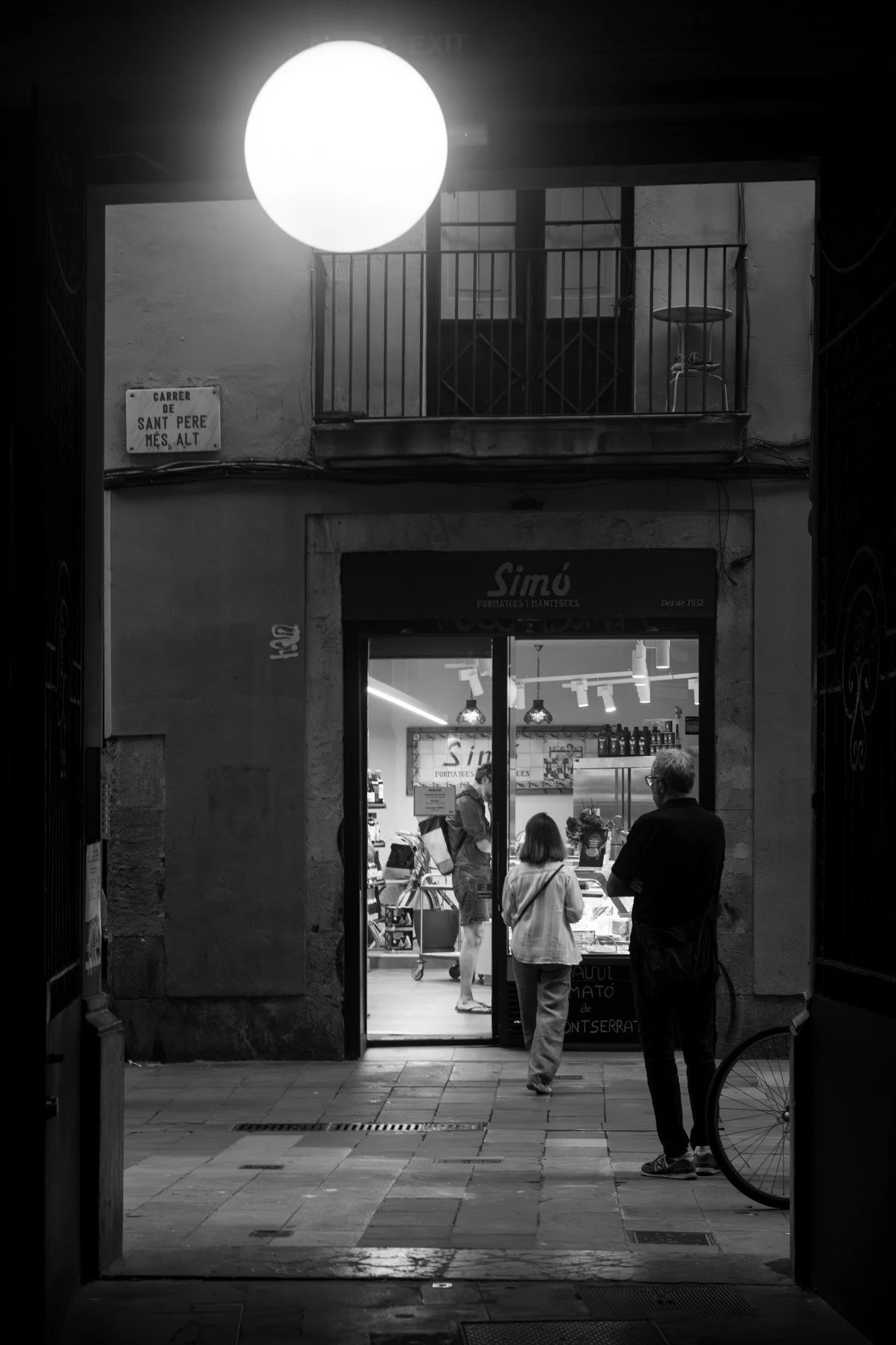 White sphere lamp glowing above the Simó cheese shop entrance on Carrer de Sant Pere Més Alt, Barcelona at night — Sony a7R IV