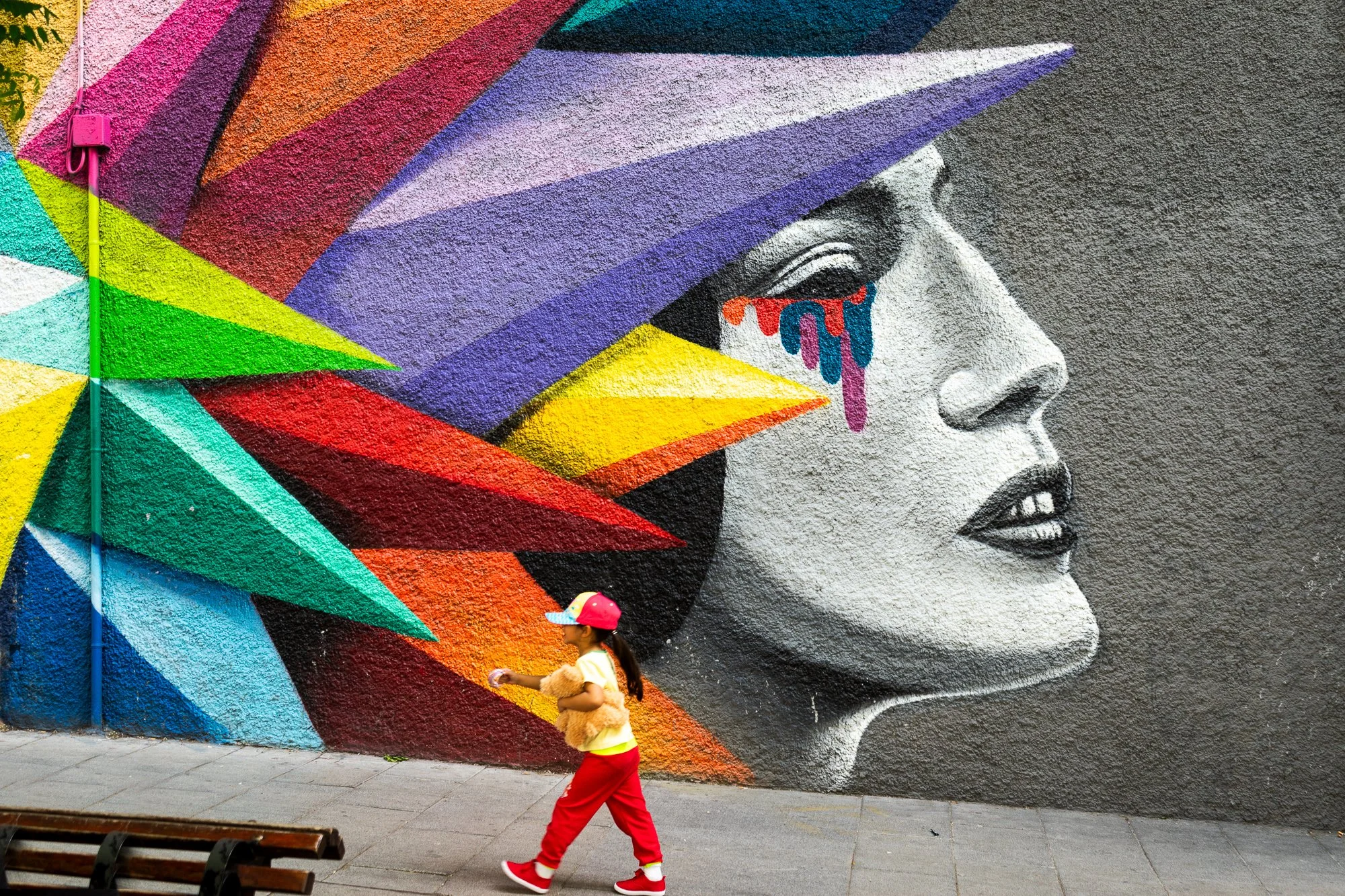 Madrid street photography: a girl in red trousers walks past a mural of a woman's face with a crown of coloured shards