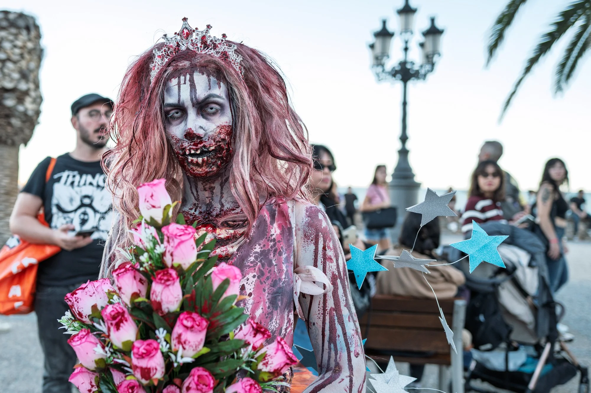 Zombie prom queen with a tiara and pink roses stares into the lens on the Sitges promenade — Leica Q3