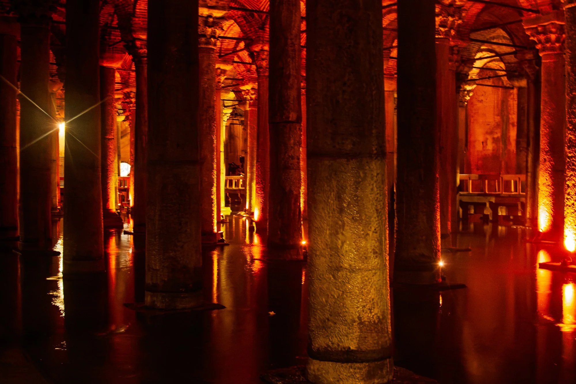 Pitted marble column lit gold in the foreground, red-lit aisles and walkways behind, Basilica Cistern, Istanbul