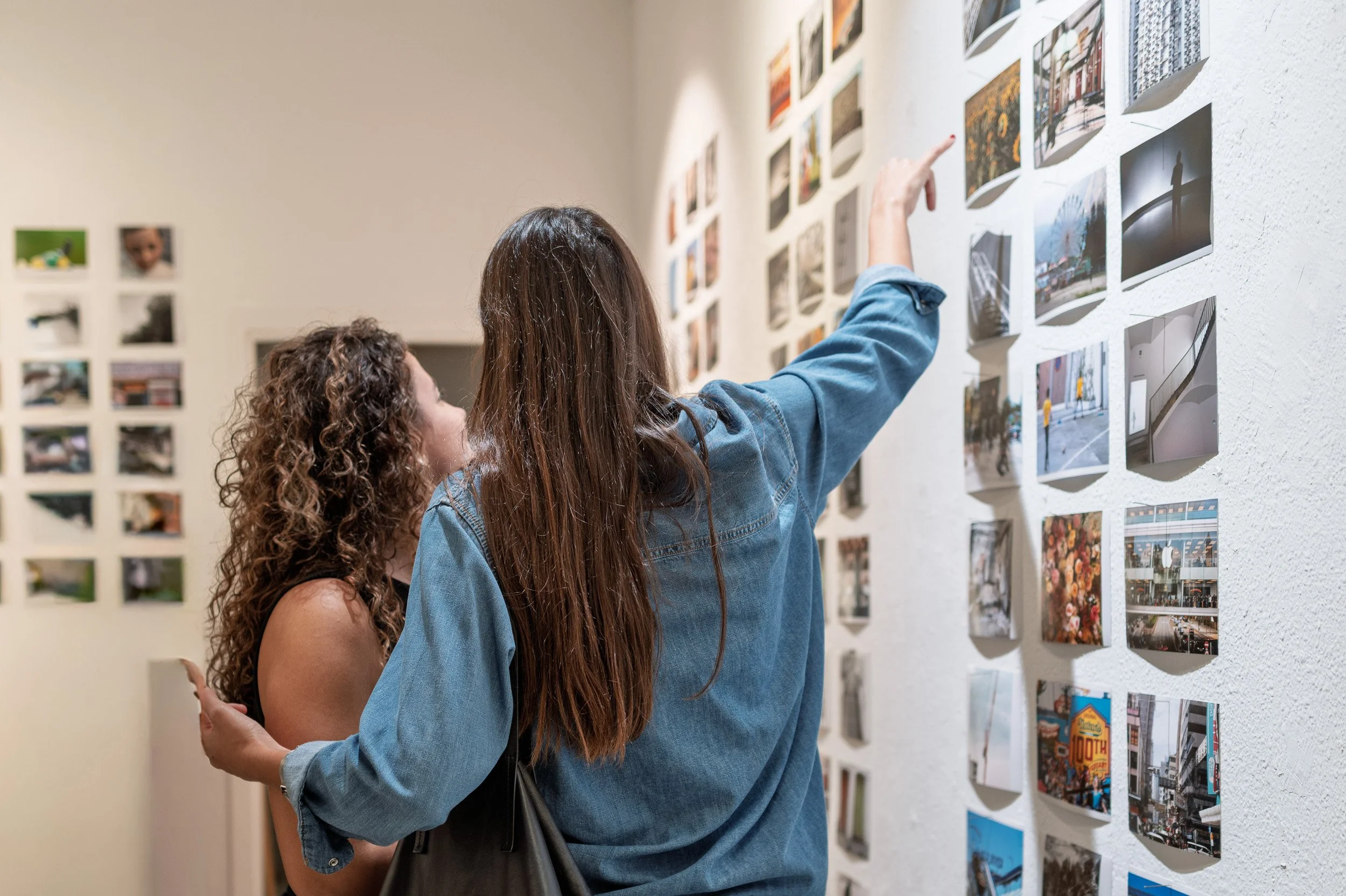 Woman in a denim shirt pointing at a print, her arm around a friend, espai[b] Barcelona — Leica Q3