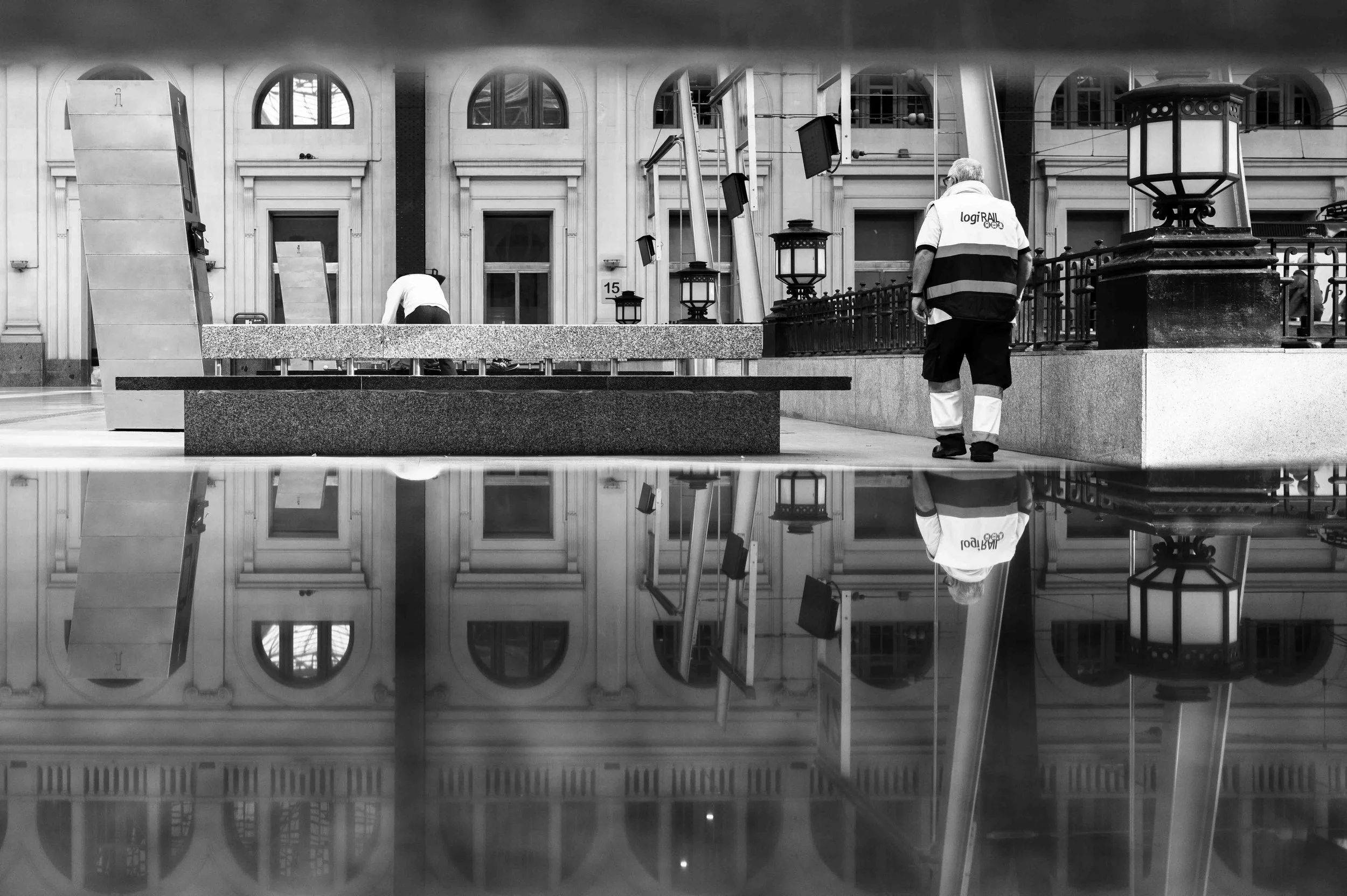 Railway worker reflected in wet pavement, black and white street photography in Barcelona – bCLPhoto