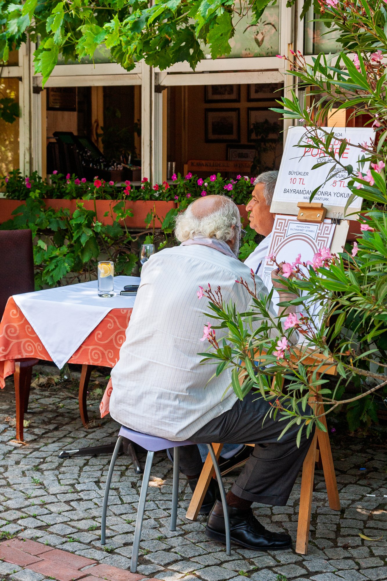 Street portrait artist drawing in pastel beside his price sign on a café terrace, Istanbul — Canon EOS 40D