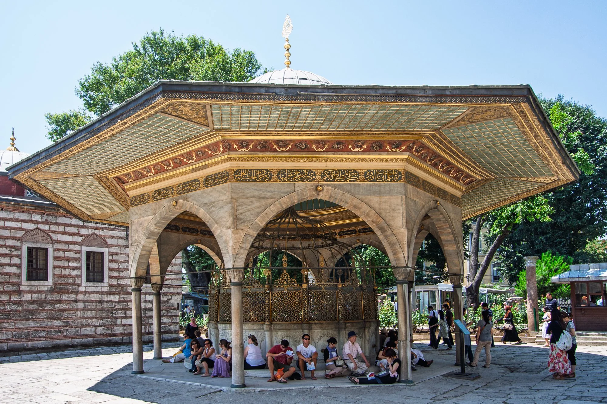 Gilded Fountain of Ahmed III with visitors resting in the shade
