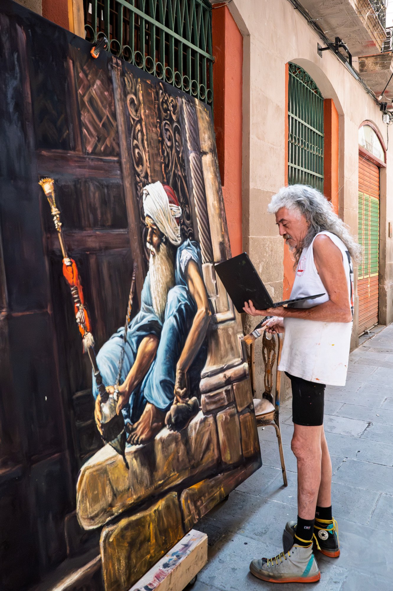 Street artist in El Born, Barcelona, painting a large portrait beside an antique doorway