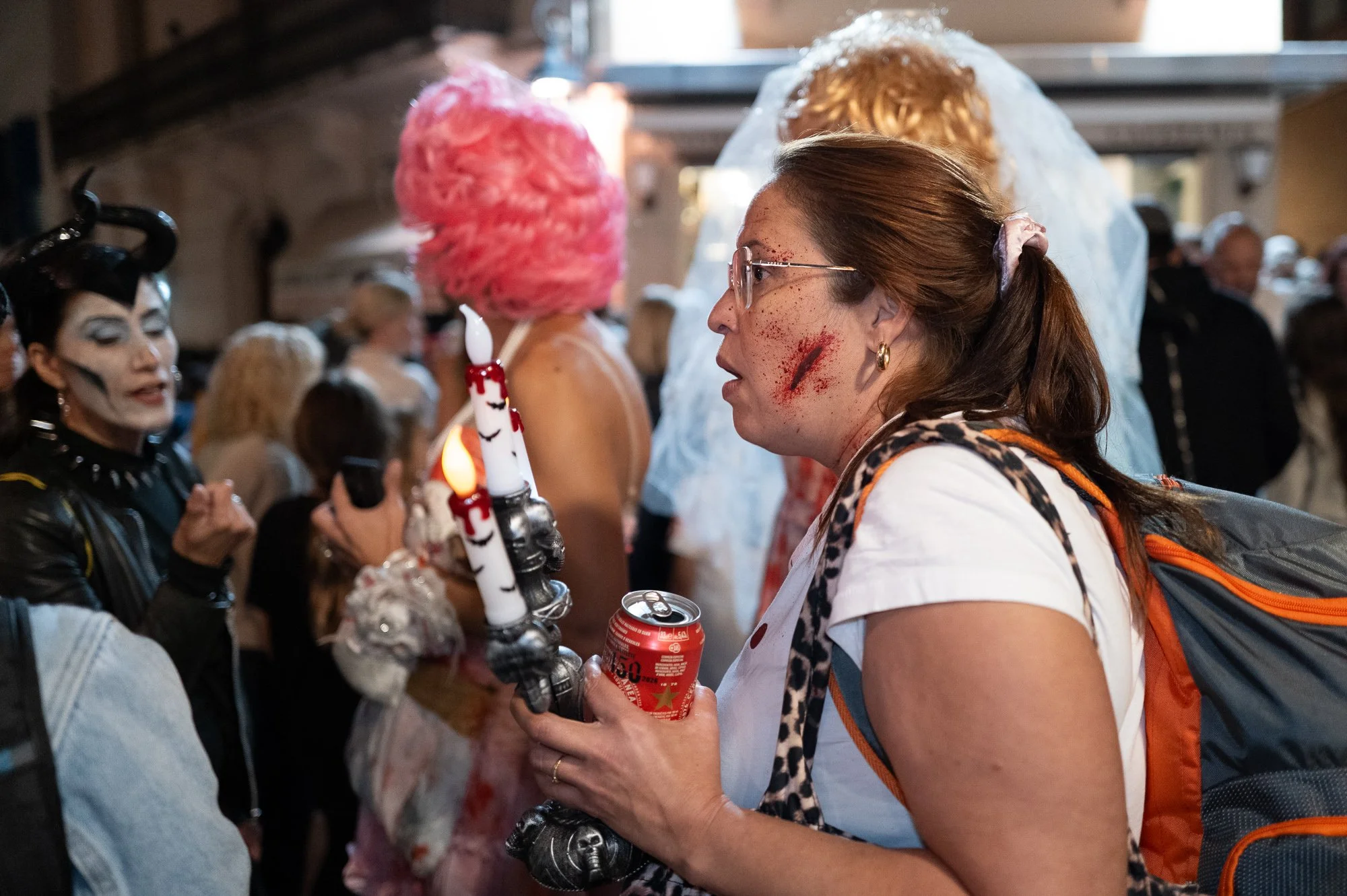 Woman with a painted scar holding a skull candelabra and a can of beer in the crowd, Sitges — Leica Q3
