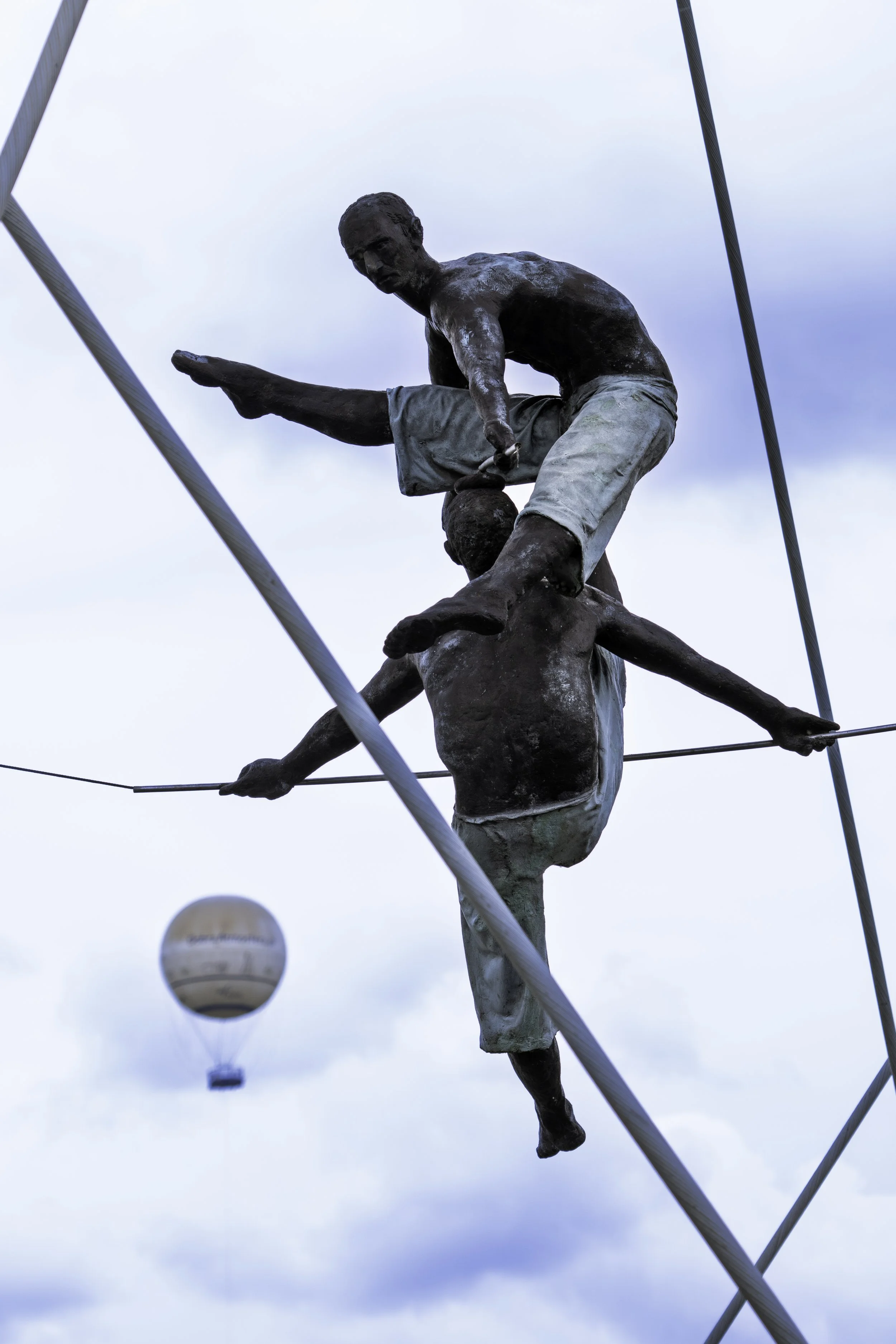 A bronze sculpture of tightrope walkers appears to share the sky with a passing hot air balloon. Kraków — bCLPhoto