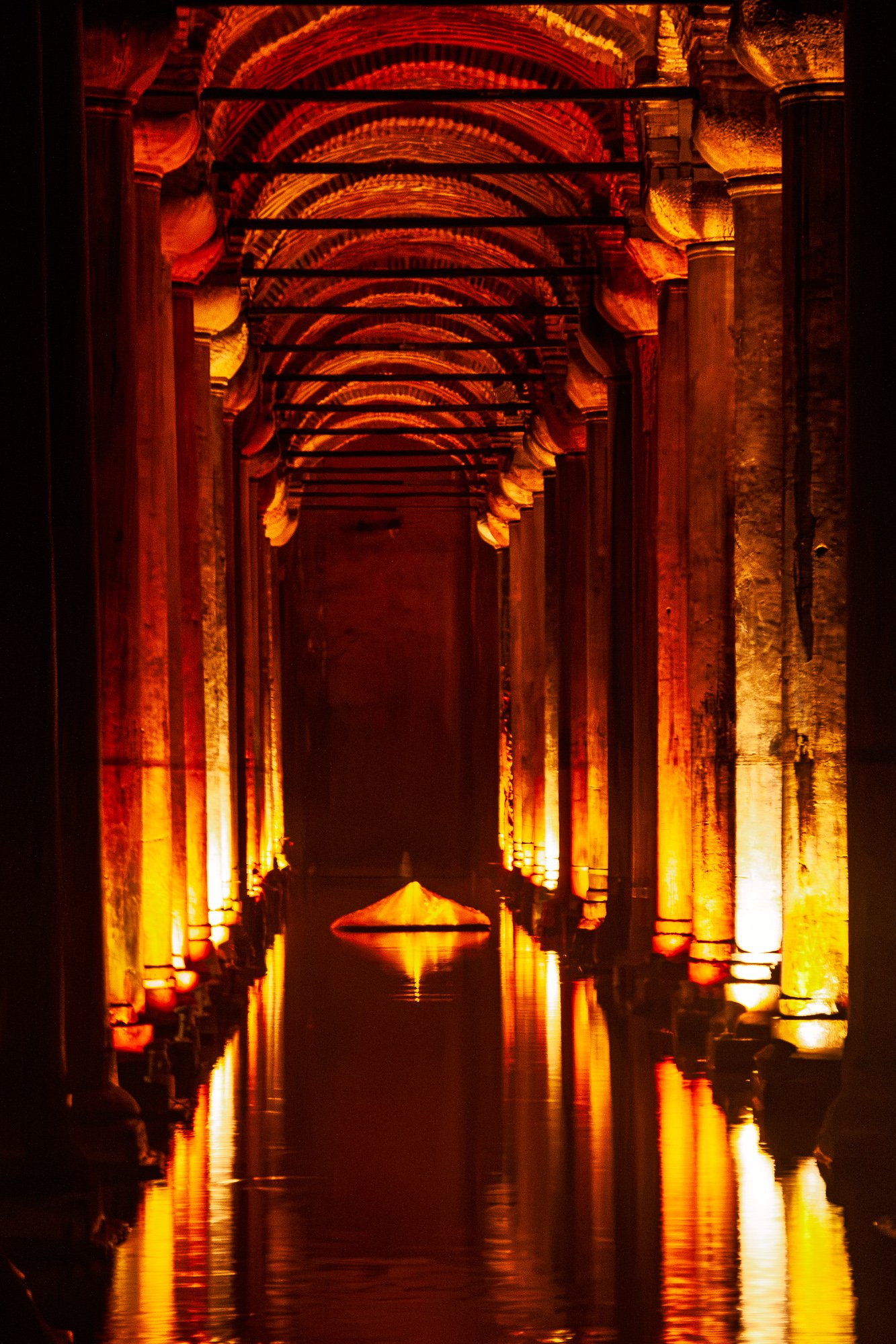 Long aisle of uplit columns and brick barrel vaults in the Basilica Cistern, a lit cone on the water at the far end