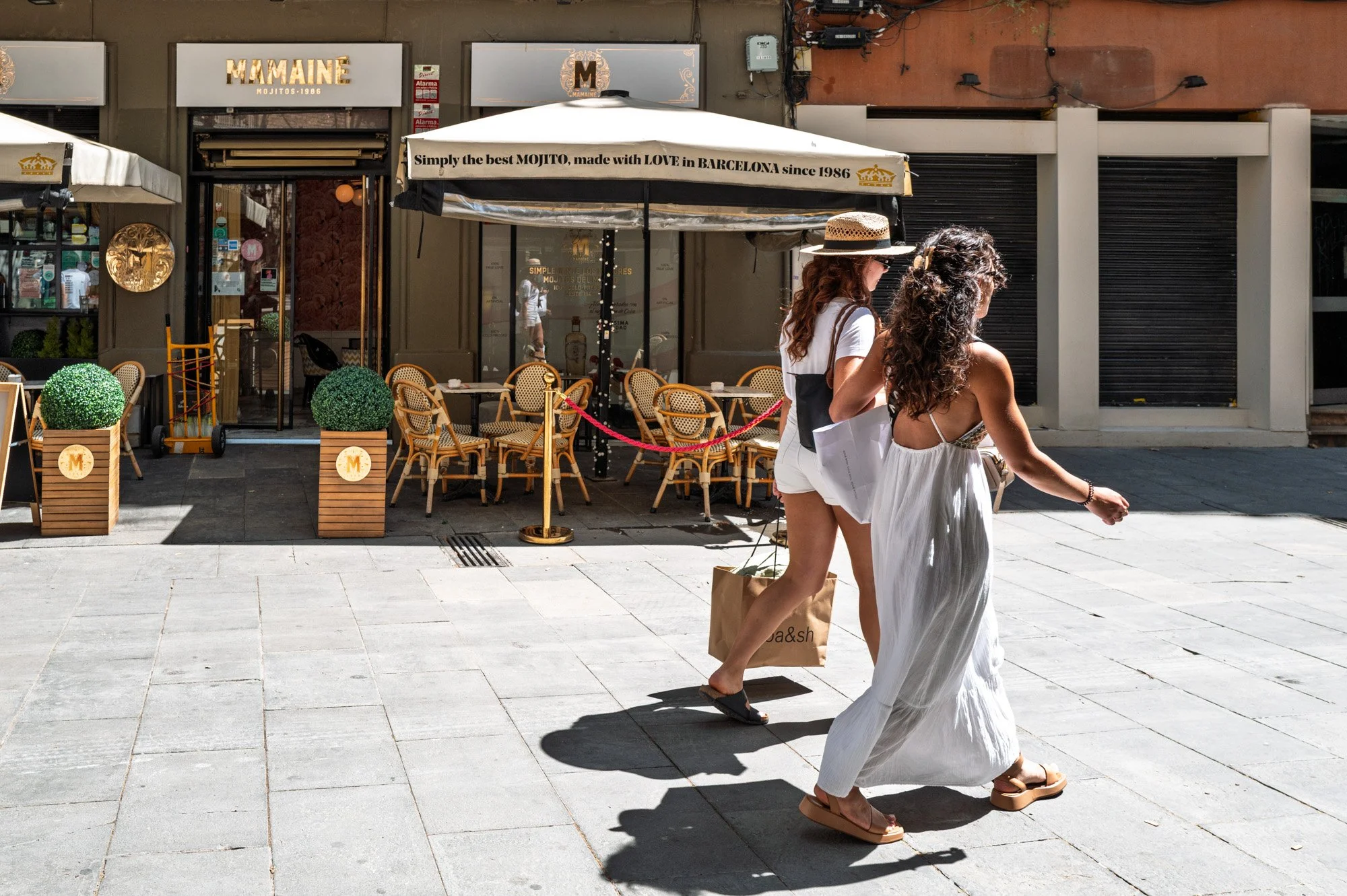 Two women in white walking past the Mamainé terrace in El Born, Barcelona