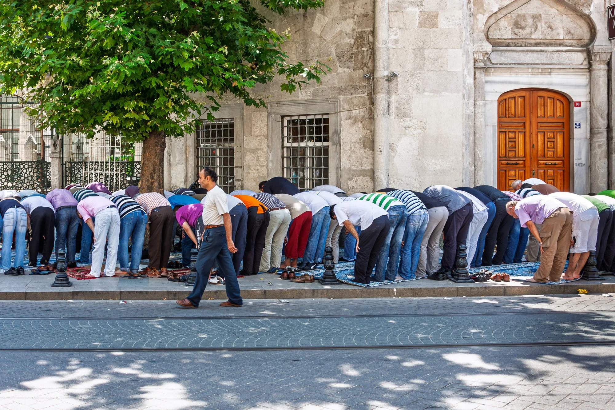 Men praying on carpets in the street of Istanbul as a passerby walks through – street photography – bCLPhoto