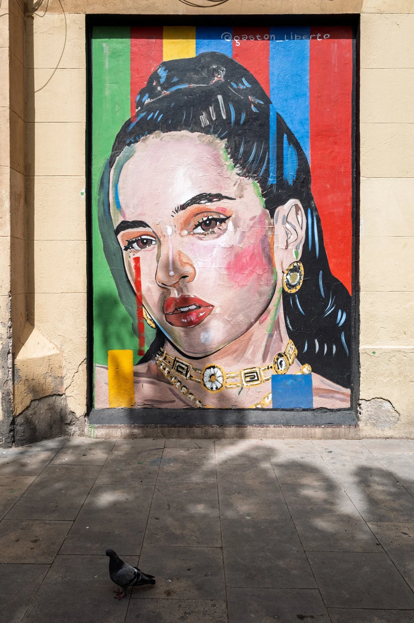 Street art mural of Spanish singer Rosalía in El Born, Barcelona, with a pigeon on the pavement below