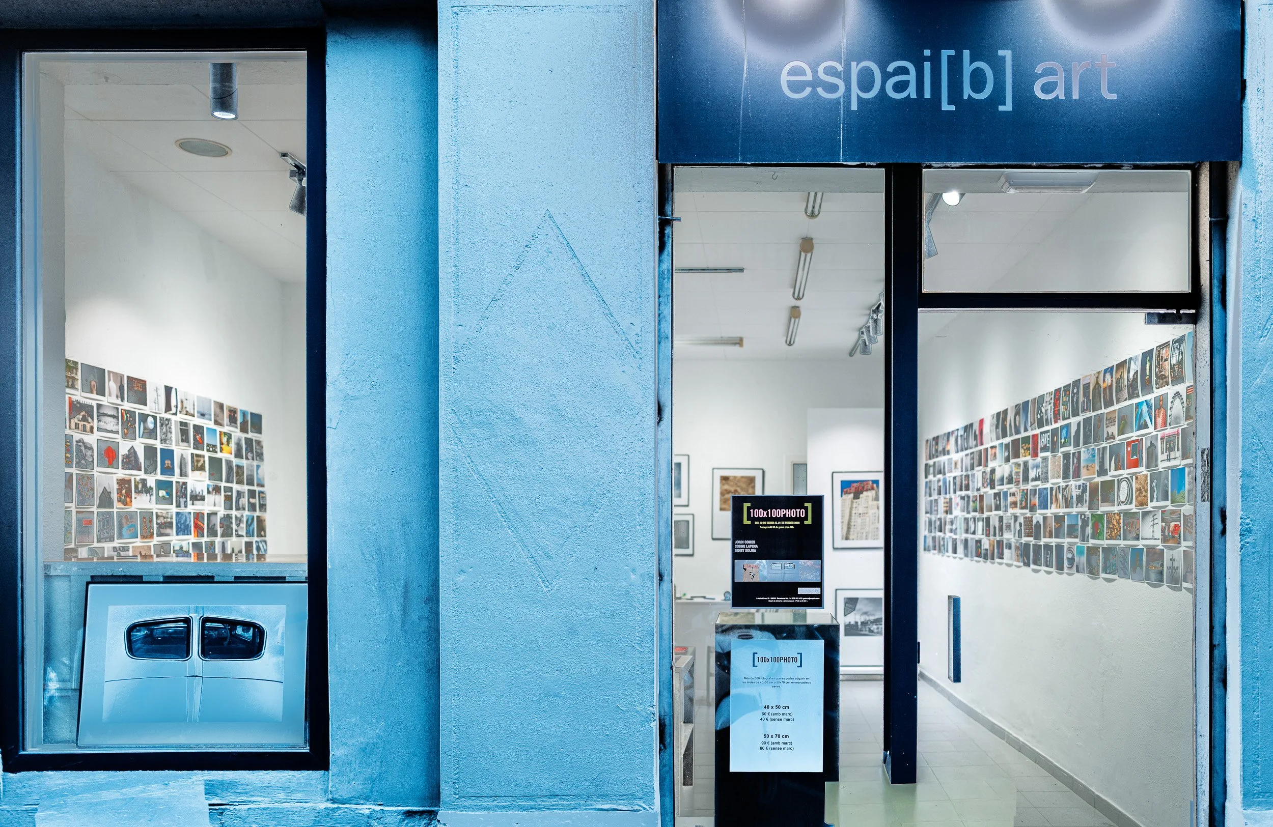 espai [b] gallery storefront in Barcelona during the 100x100PHOTO exhibition, January 2025, with walls of small prints visible inside.