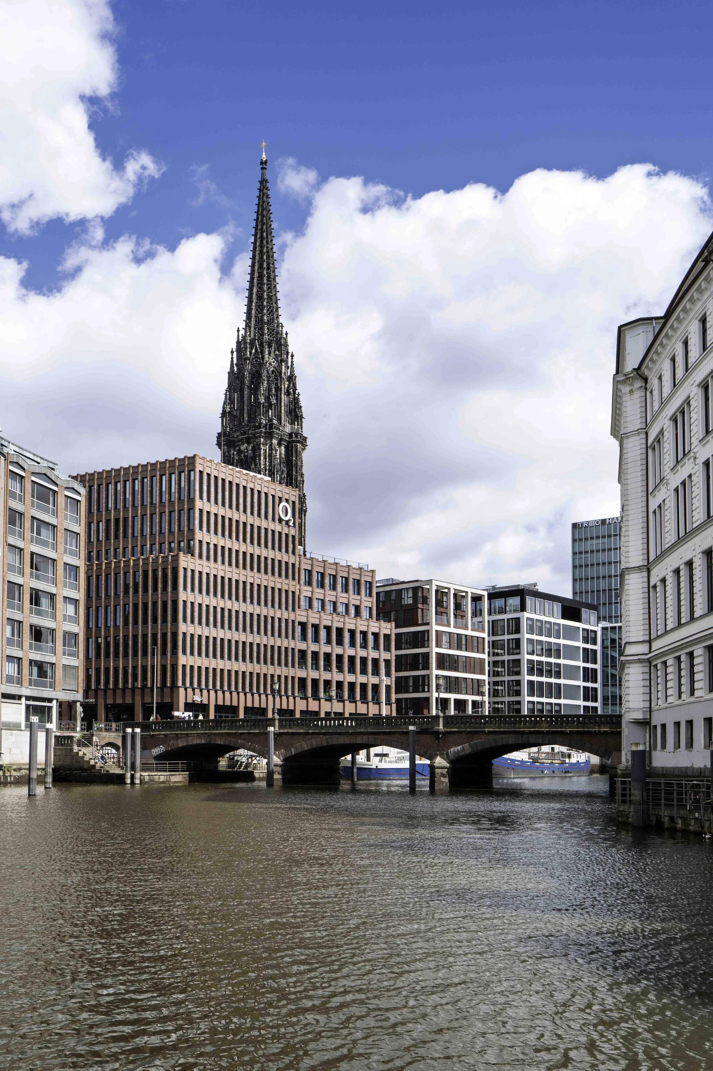 Stone bridge over Hamburg canal with St Nikolai church spire rising behind modern buildings — Leica Q3