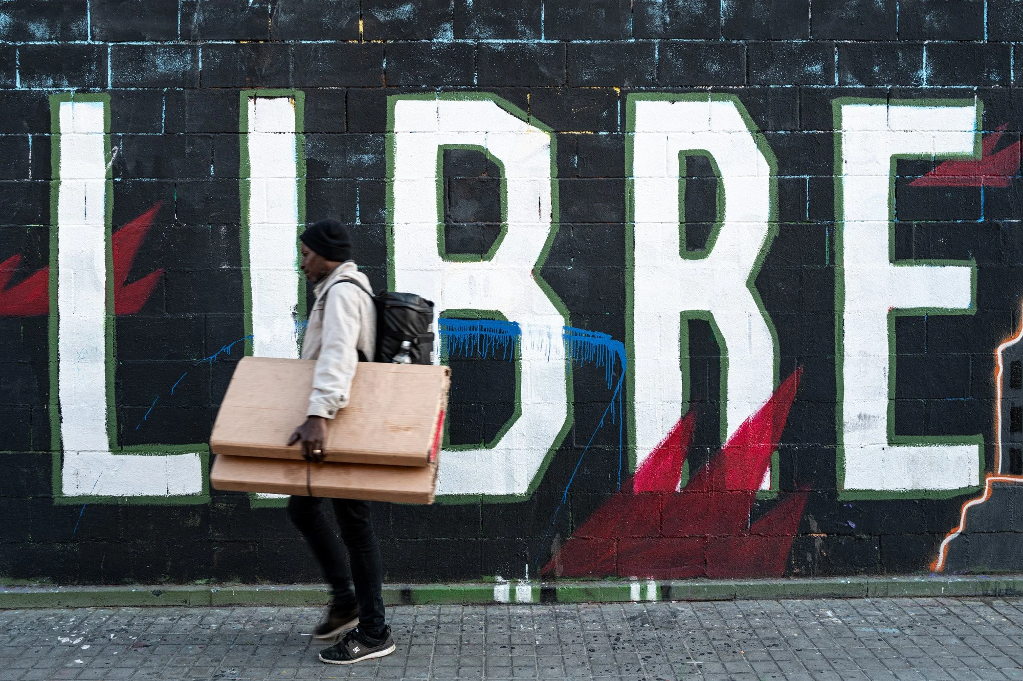 Man carrying wooden boards past LIBRE graffiti in Barcelona, street photography — Leica Q3 — bCLPhoto