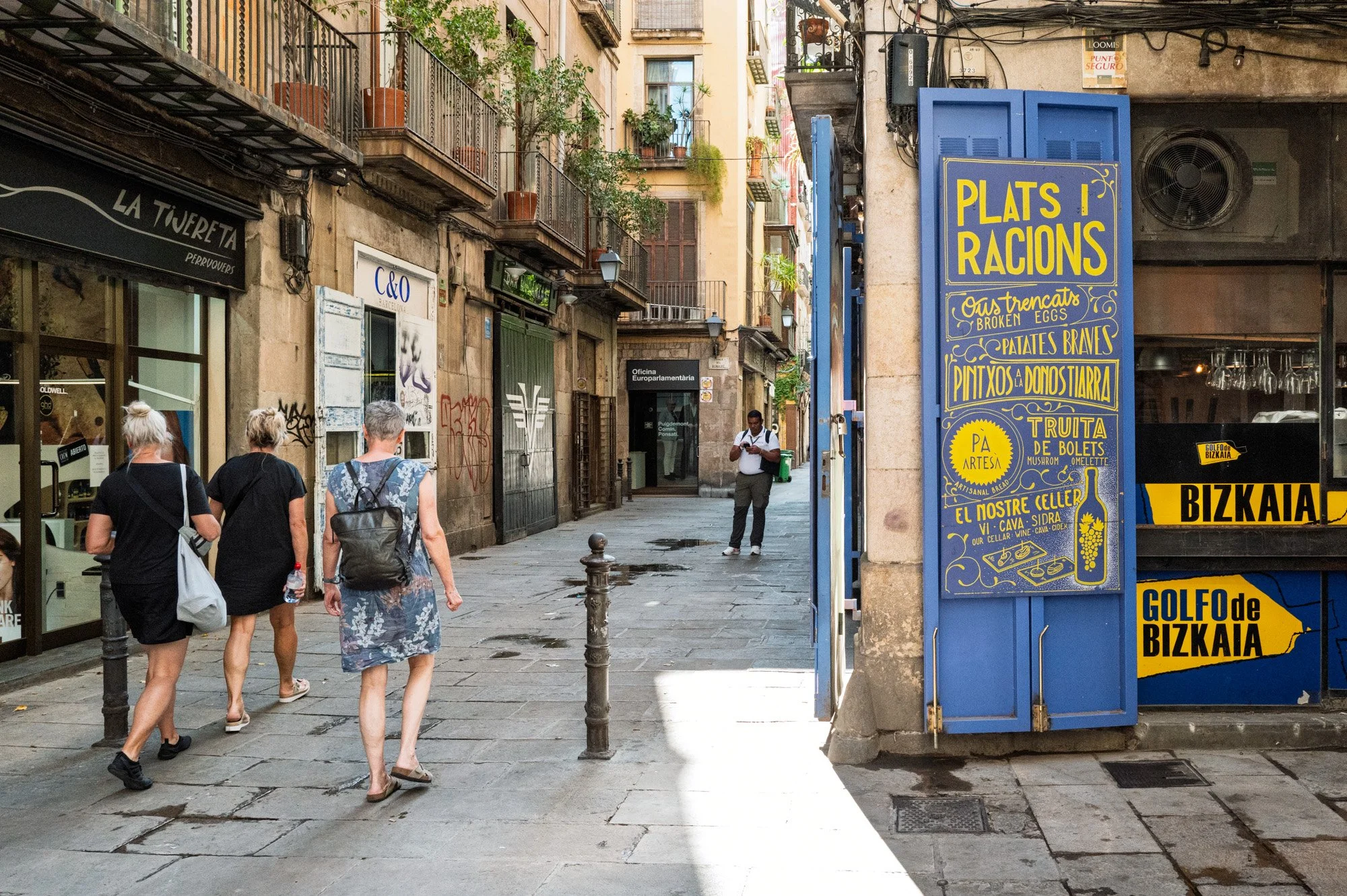 Three women reading a hand-painted Plats i Racions menu board, El Born — Leica Q3