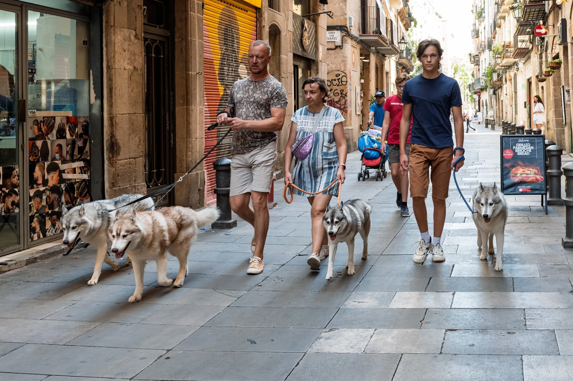 Family walking four husky dogs through a narrow street, El Born street photography — Leica Q3