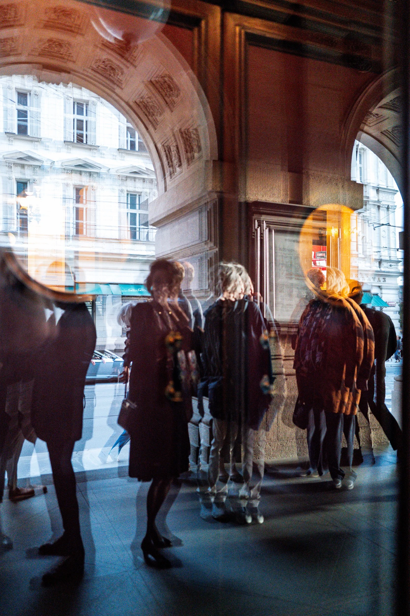 Visitors under the National Theatre arches, doubled by reflections in the glass, Prague — Leica Q3