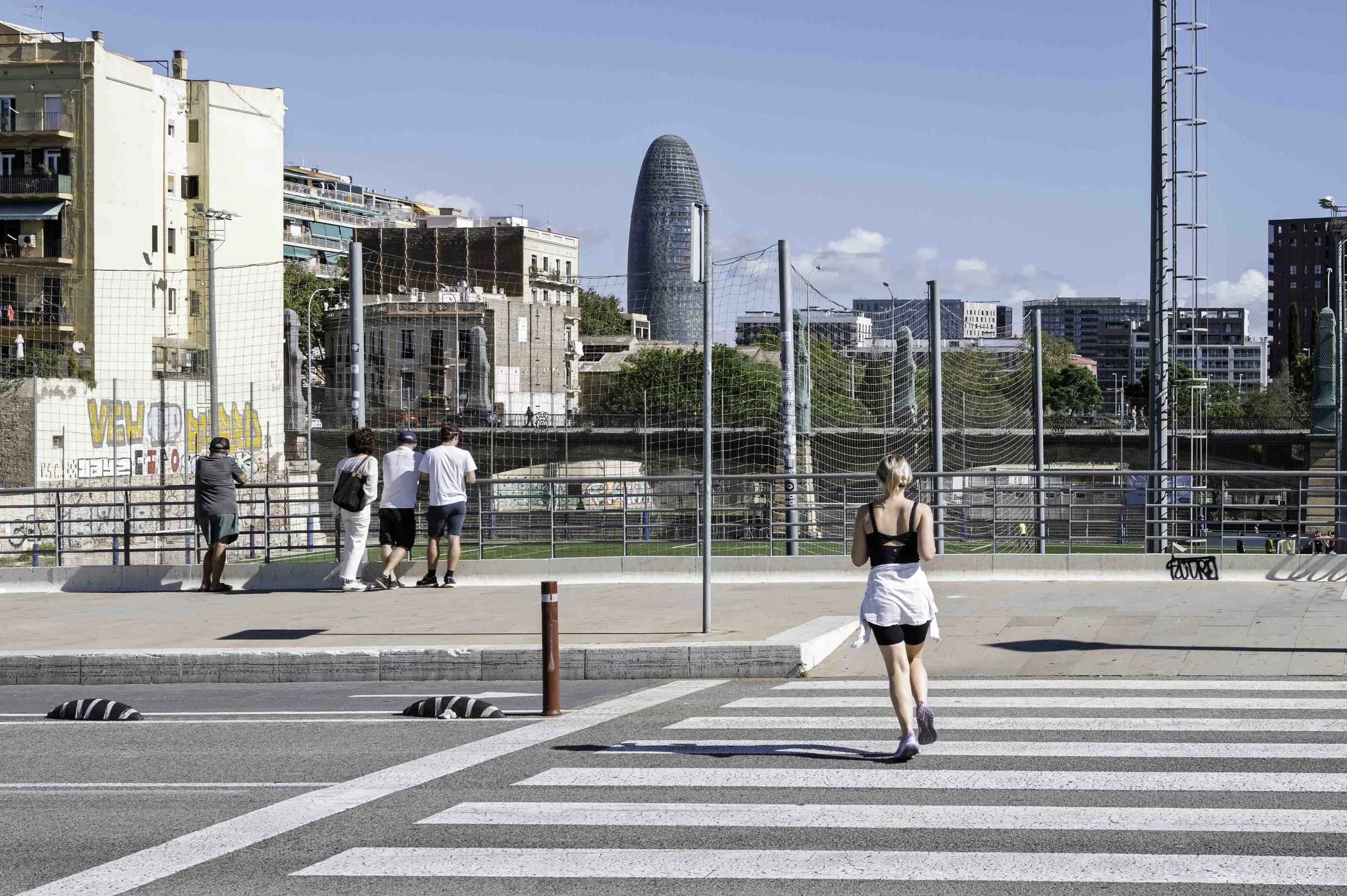 Woman jogging across a zebra crossing in Poblenou Barcelona with Torre Agbar rising in the background — Leica Q3