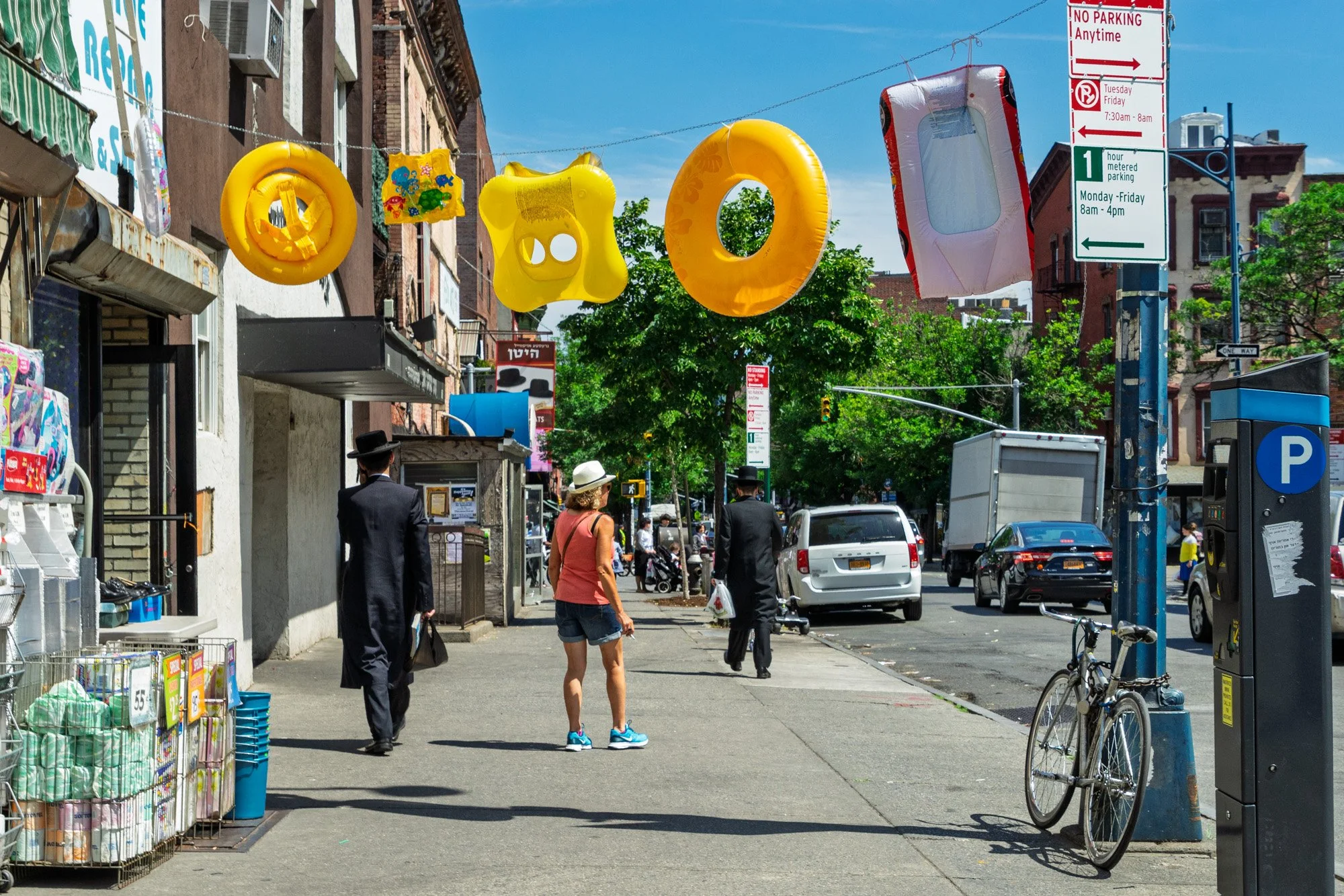 Inflatable pool rings hanging above Lee Avenue with pedestrians, South Williamsburg Brooklyn — Sony a7II