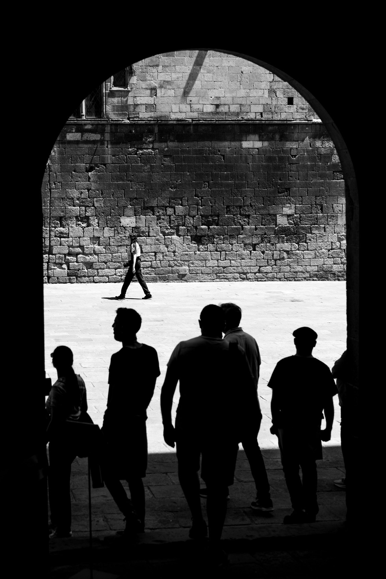Silhouettes of people under a stone arch in Barcelona's Gothic Quarter, black and white street photography — Sony a7R IV