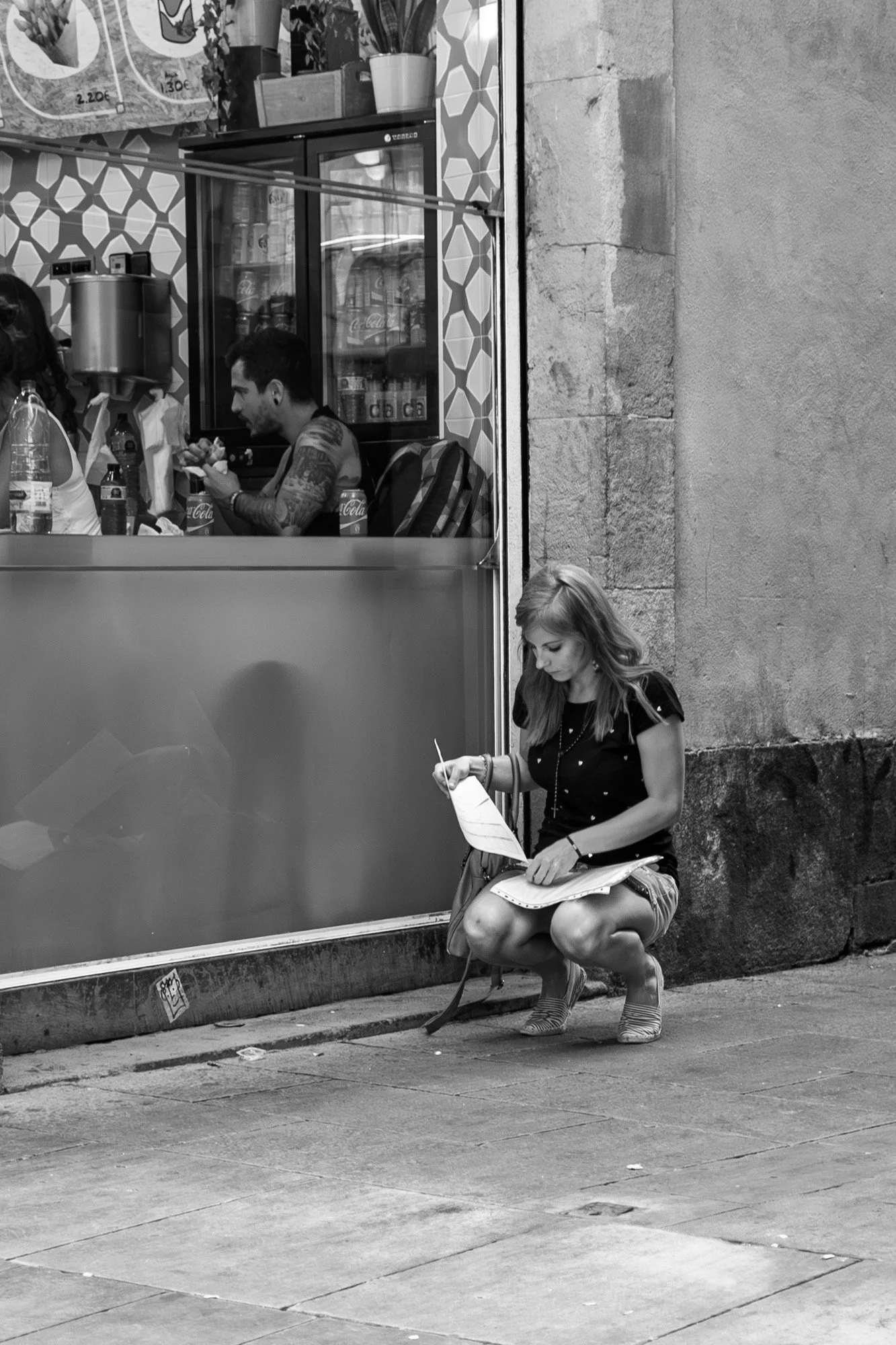 Young woman crouching on the pavement writing in a notebook outside a bar, Gothic Quarter Barcelona — Leica Q3