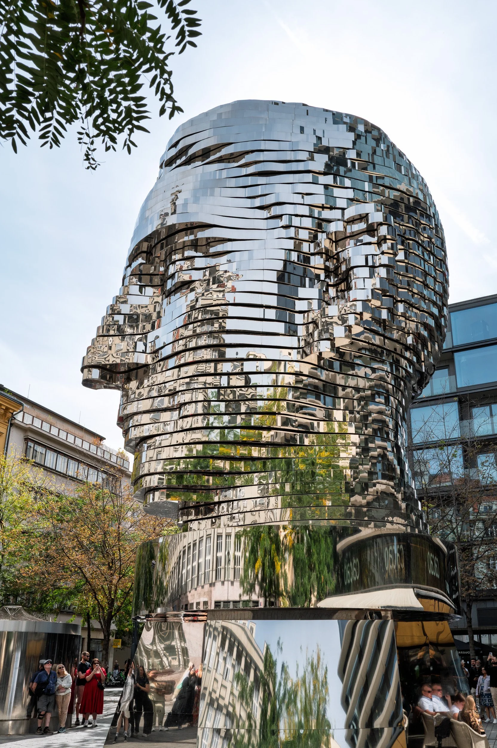 David Černý's mirrored Head of Franz Kafka reflecting buildings and trees, visitors filming below, Prague — Leica Q3