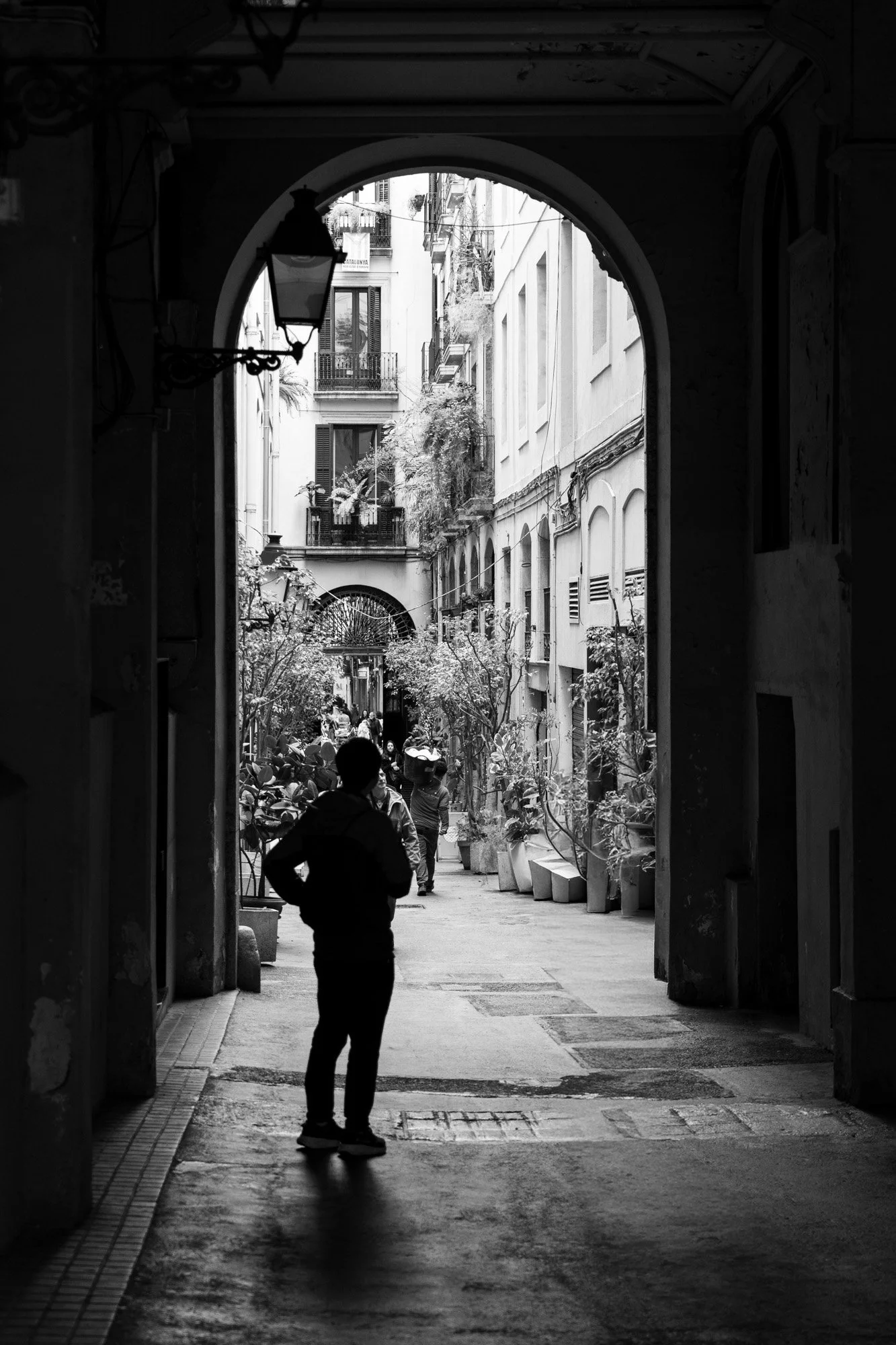 Silhouette standing in a Gothic arch, sunlit courtyard behind, Barcelona Gothic Quarter — Leica Q3