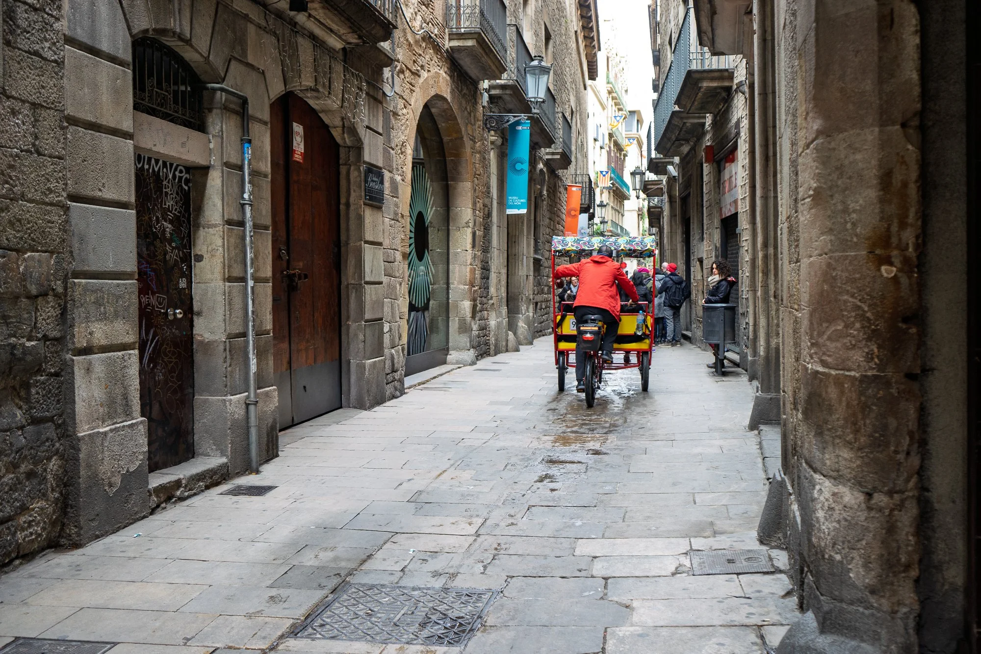 Red pedicab passing through narrow El Born street — Leica Q3