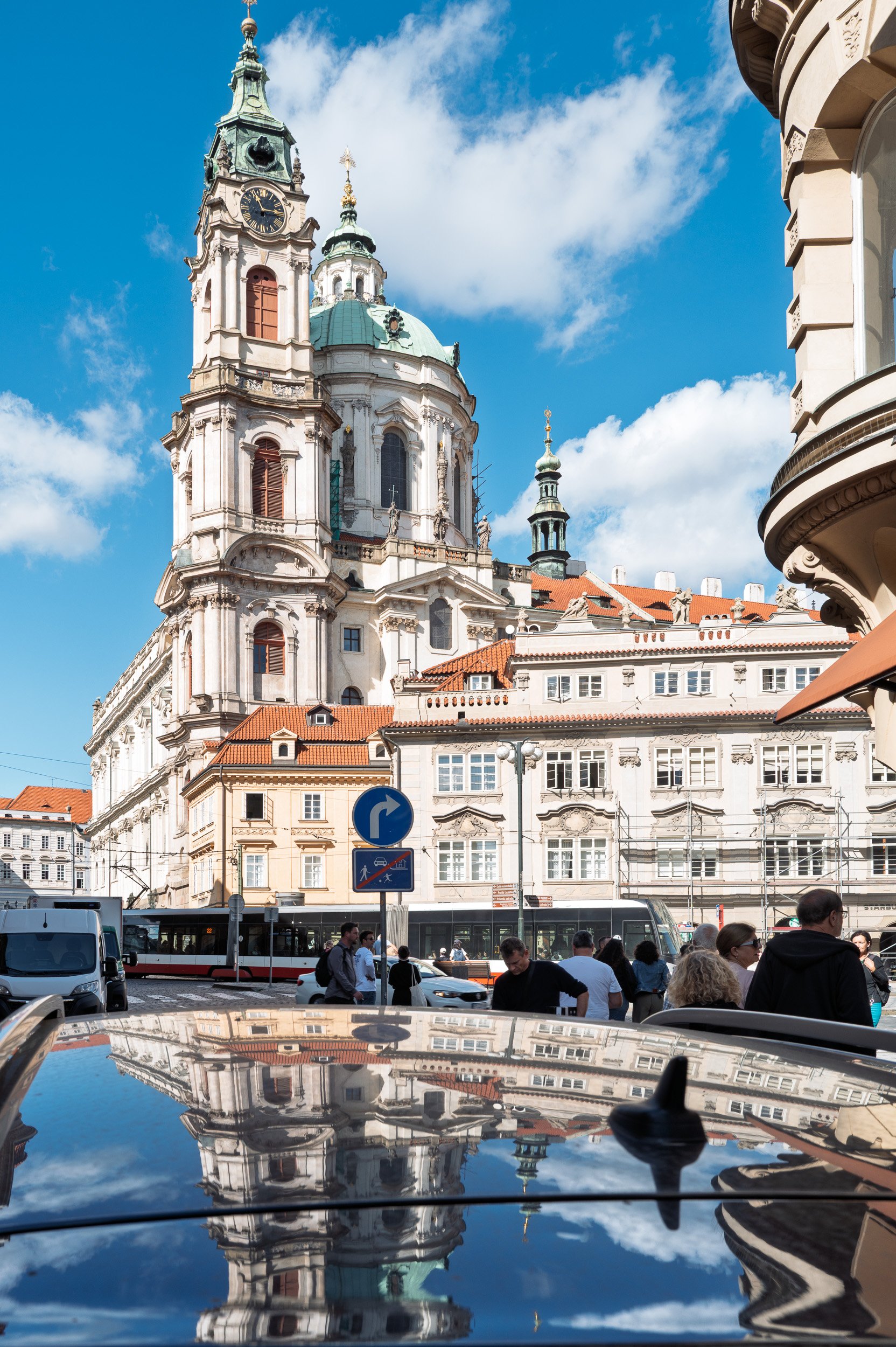 Church of St Nicholas reflected upside down on a black car roof, tram passing, Malá Strana, Prague — Leica Q3