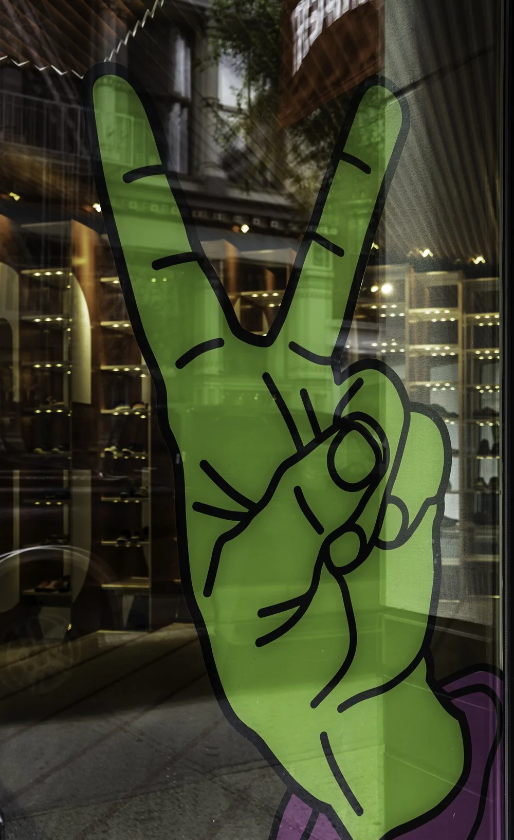 Victory sign with fingers on the shop window seen behind, at the same time as the reflection of the buildings opposite, Street photography in Barcelona – bCLPhoto