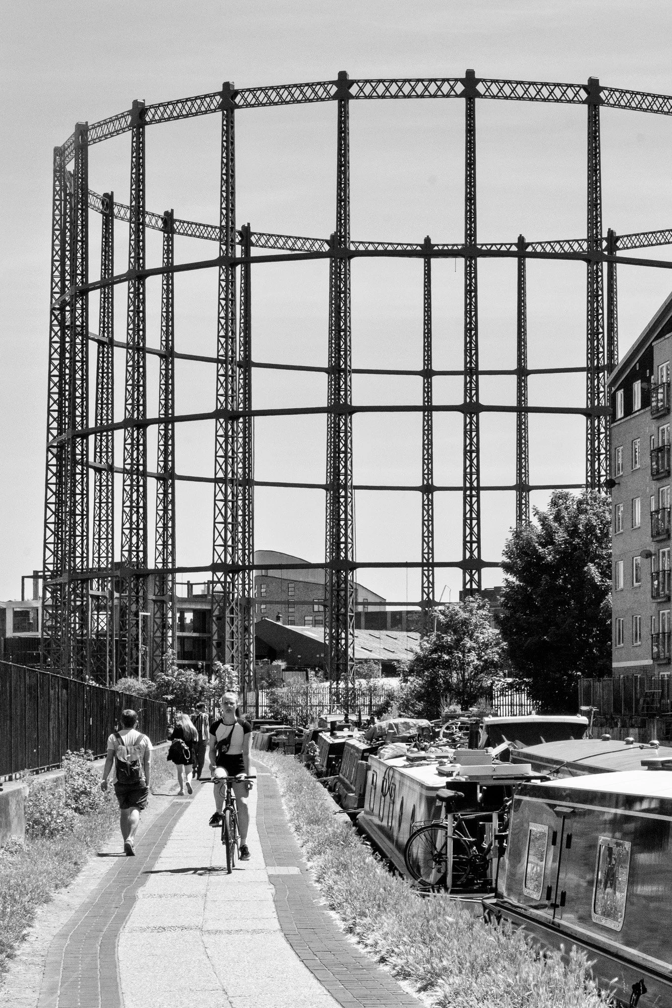 Victorian gasometer frame rising above the Regent's Canal towpath with cyclists and narrowboats, East London — bCLPhoto