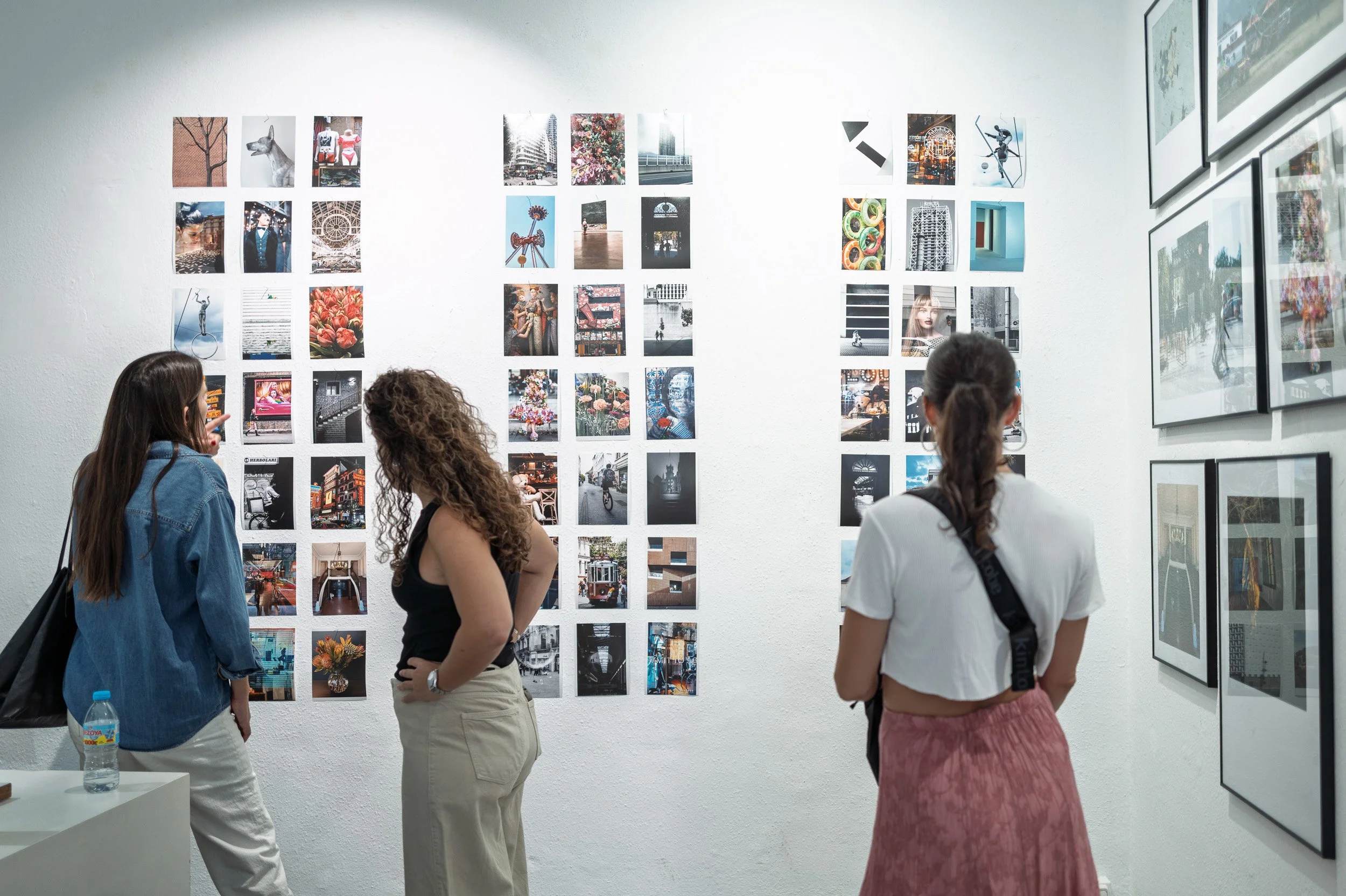 Three visitors looking at a wall of vertical prints, one pointing, espai[b] Barcelona — Leica Q3