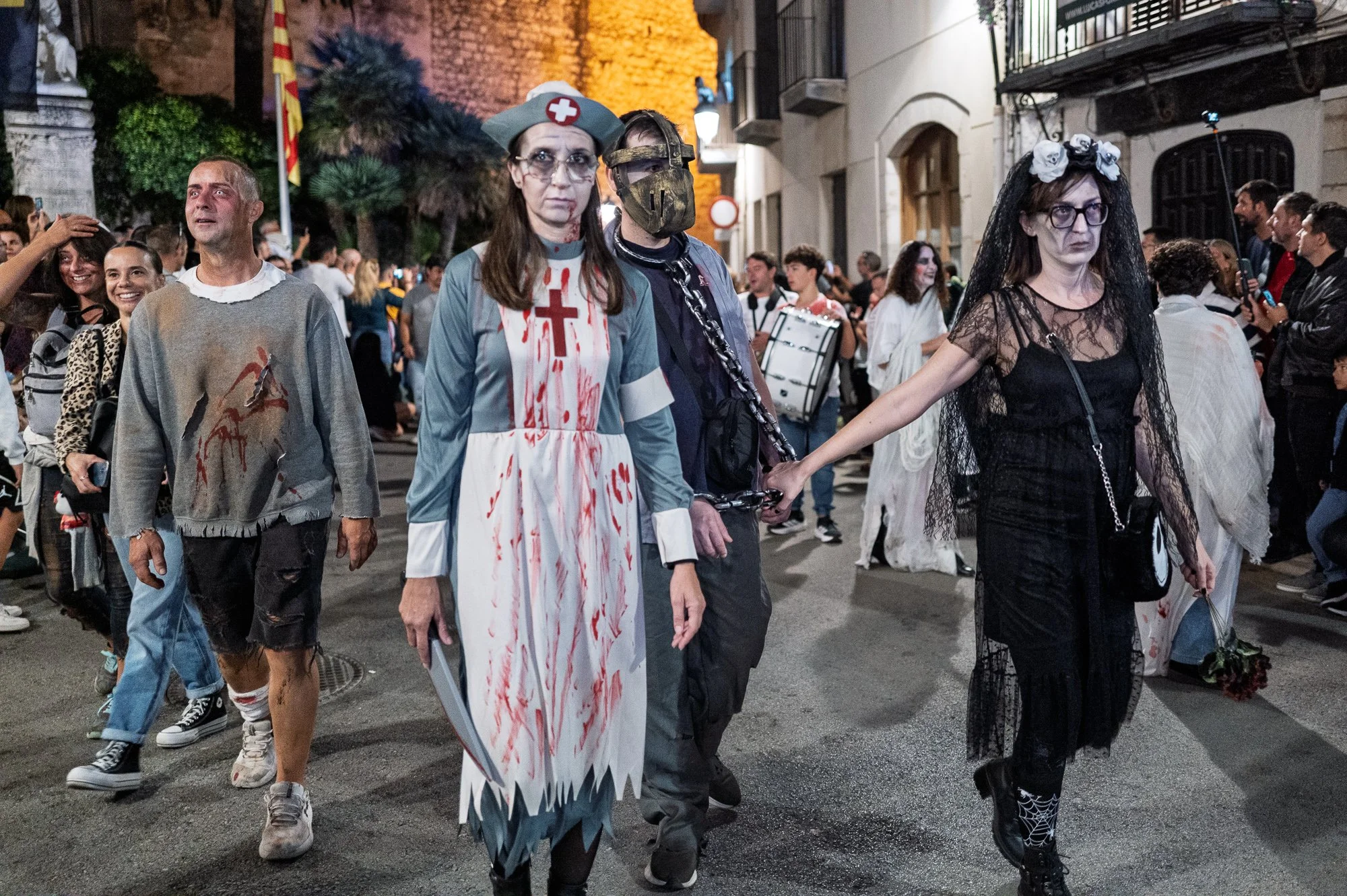 Sitges Zombie Walk at night: nurse with a cleaver, a chained masked man and a woman in black lace — Leica Q3