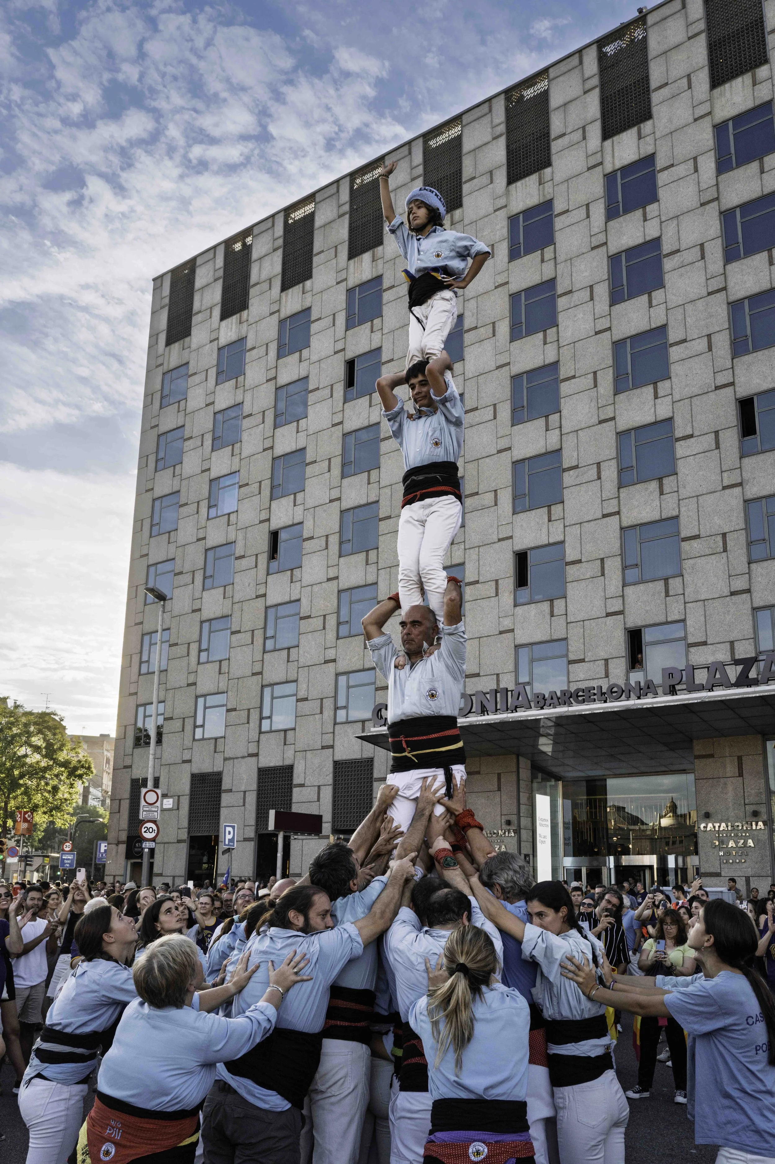 Castellers human tower in front of Las Arenas de Barcelona in September, child at the top raising one arm with crowd watching — Leica Q3