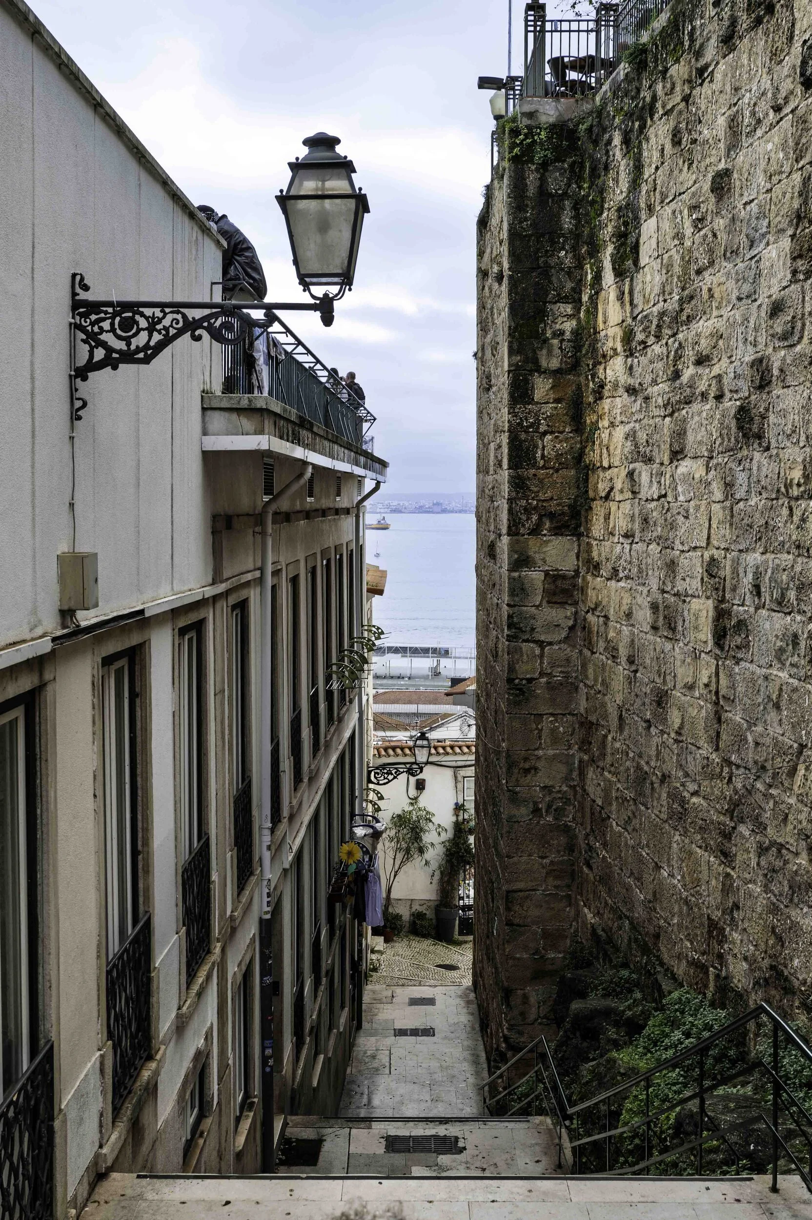 Narrow staircase passage in Alfama with ornate lamppost and glimpse of the Tagus, Lisbon — Leica Q3