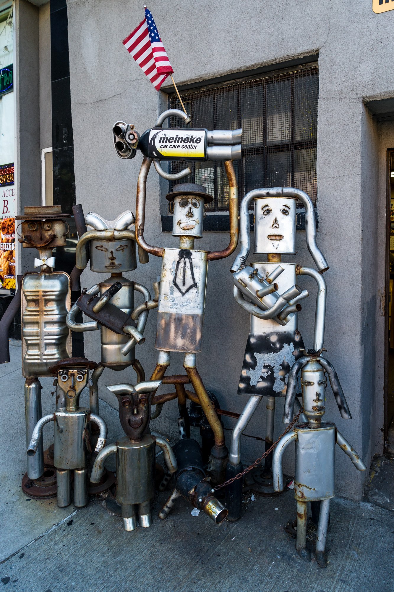 Metal robot sculptures made from exhaust pipes outside a Meineke shop, Brooklyn — Sony a7II
