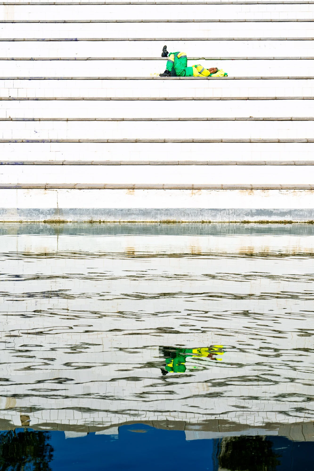 Worker resting on white steps with water reflection – street photography – bCLPhoto