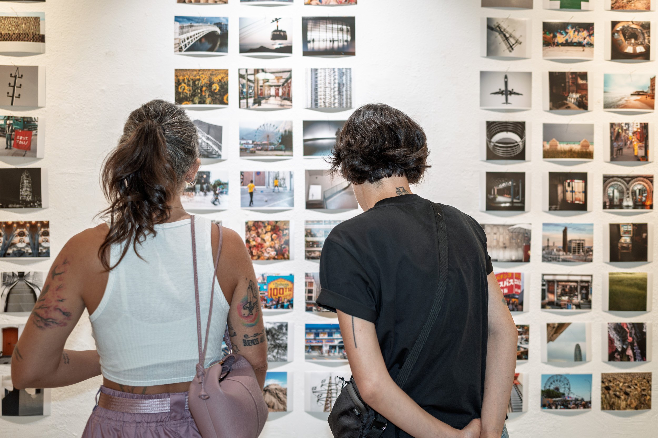 Two visitors seen from behind studying a wall of small photographs, espai[b] Barcelona — Leica Q3