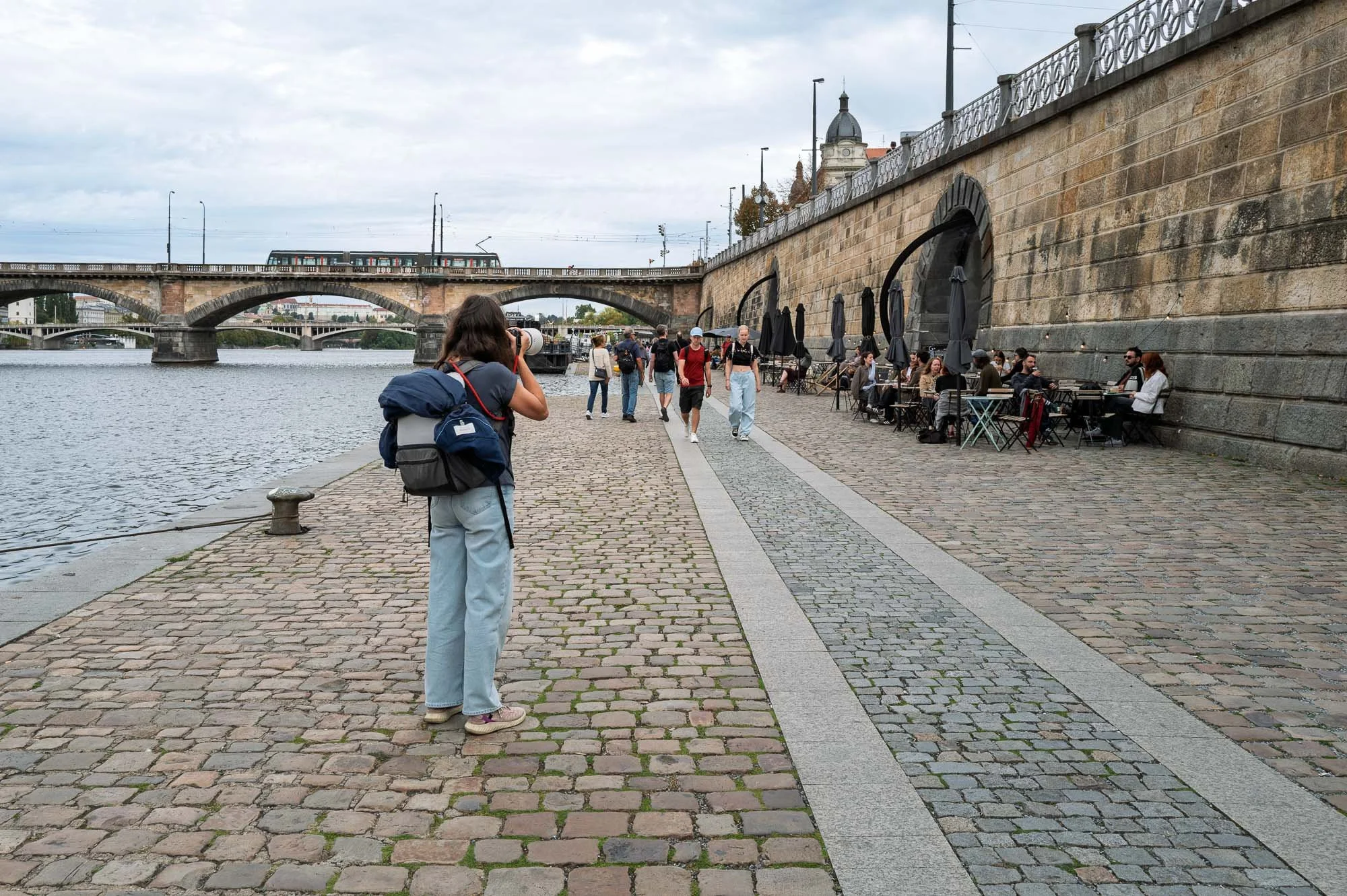 Young woman with a white telephoto lens on the Vltava embankment, Prague street photography — Leica Q3