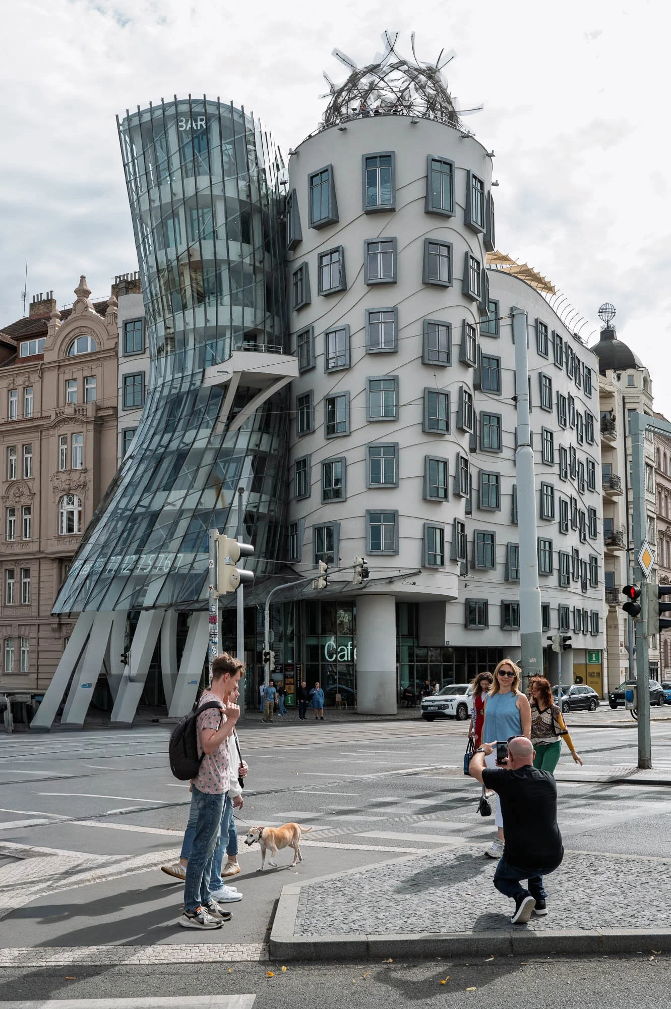 Man crouching to photograph three women in front of the Dancing House, Prague — Leica Q3