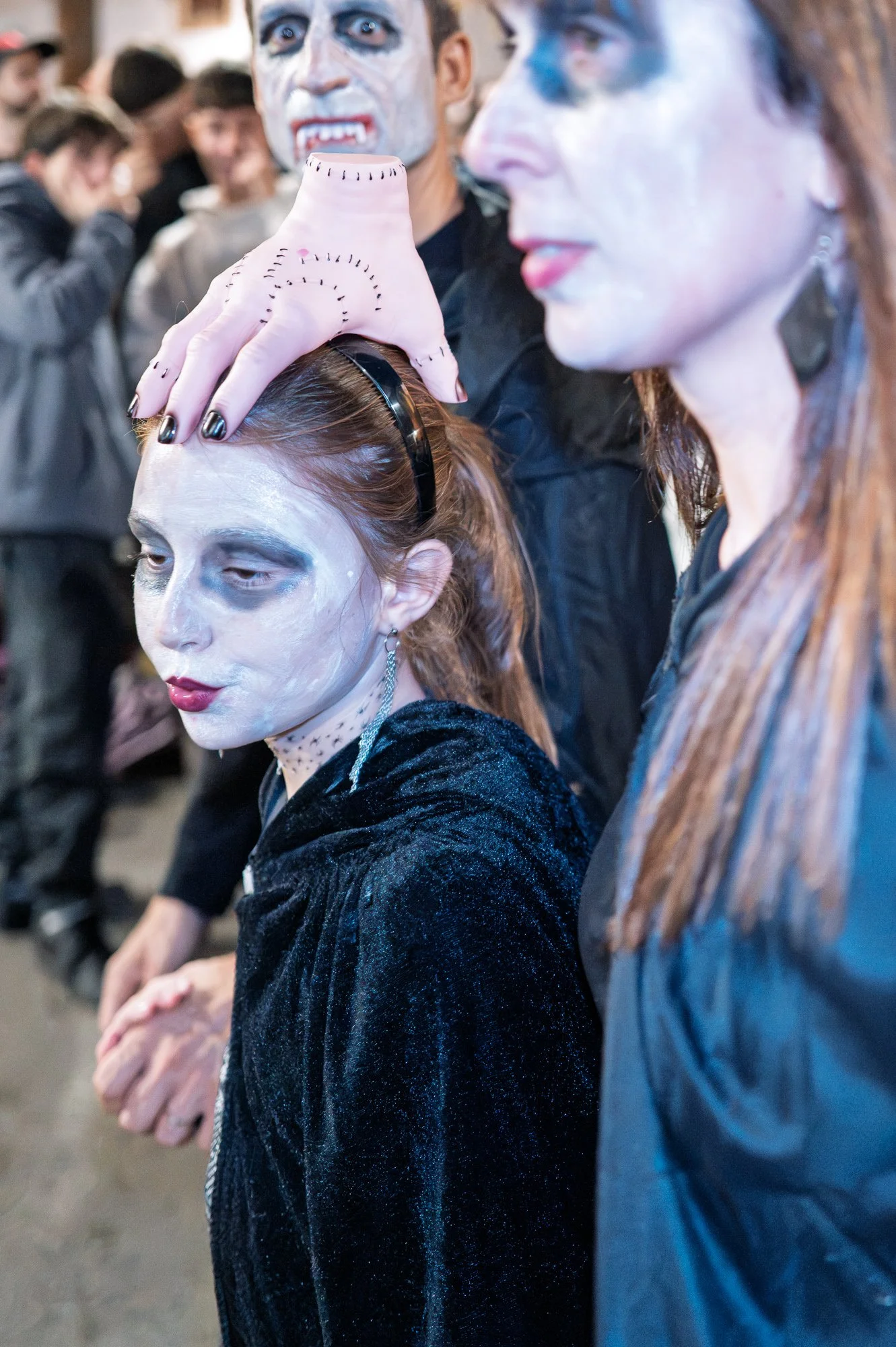 Girl in white face paint wearing a severed-hand headband, a vampire behind her, Sitges — Leica Q3