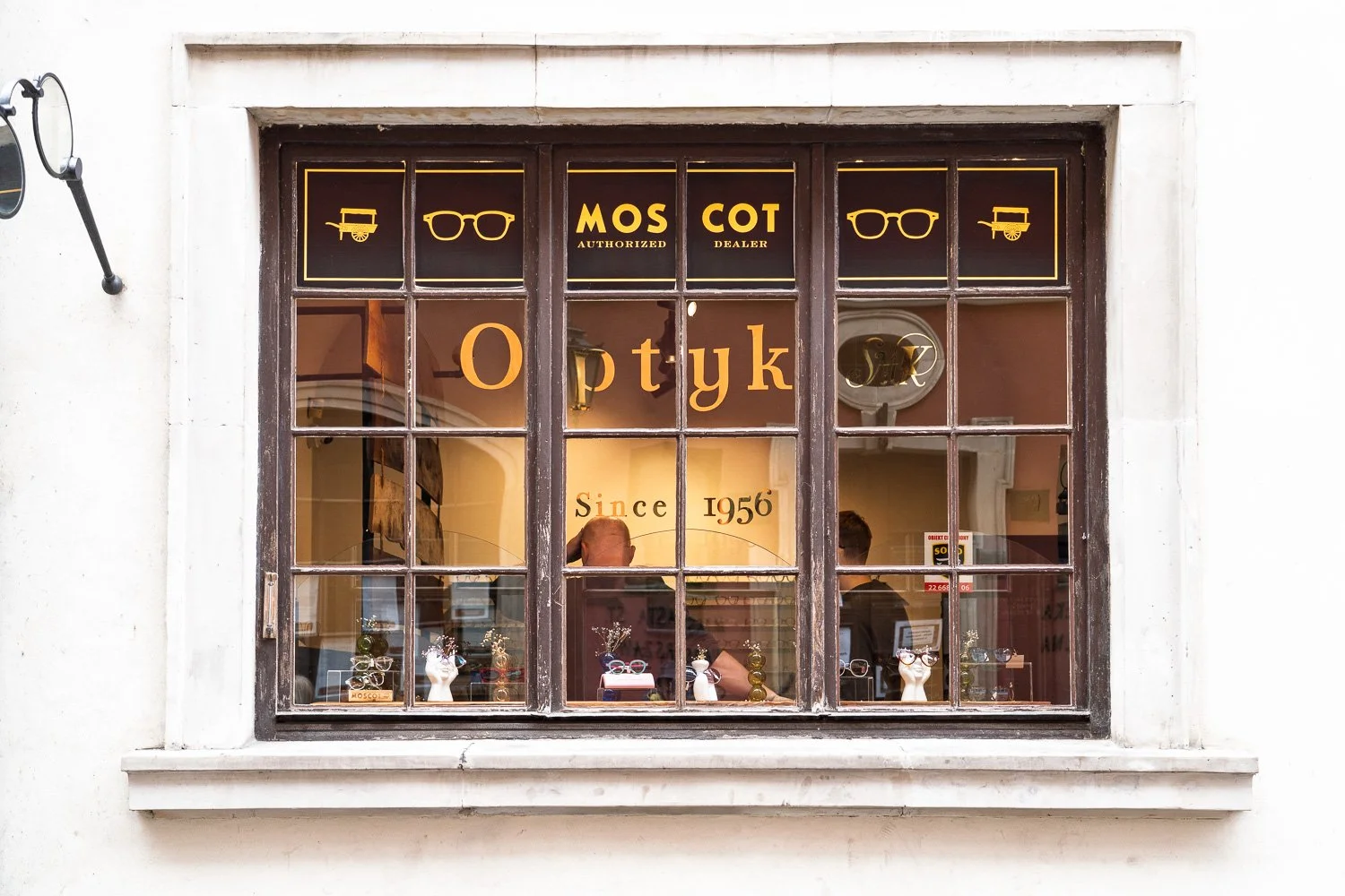 Optician's shop window with gold "Optyk" lettering and an older man inside, Warsaw Old Town — Sony a7R IV