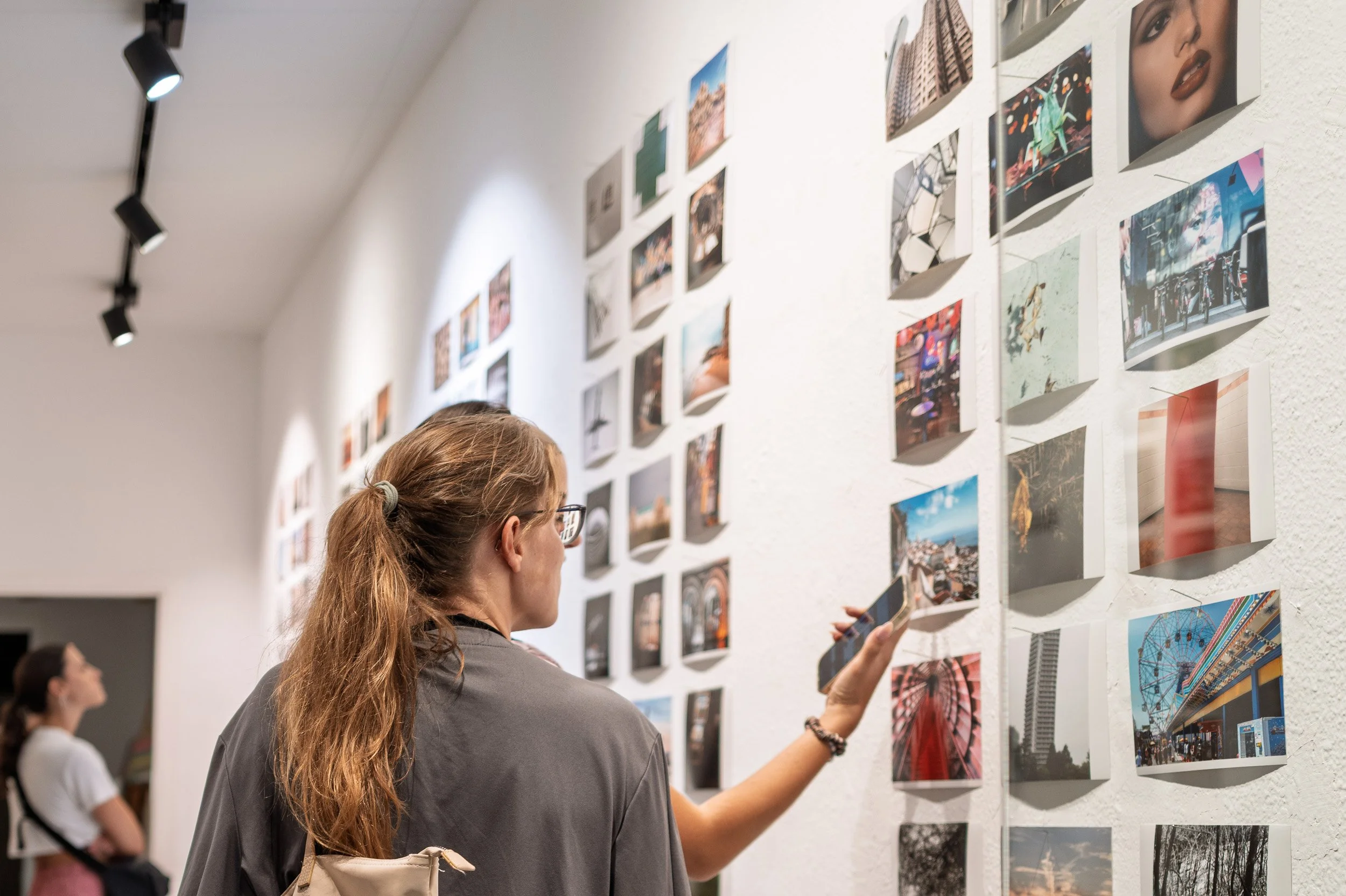 Visitor holding up a phone to photograph a print on the gallery wall, espai[b] Barcelona — Leica Q3