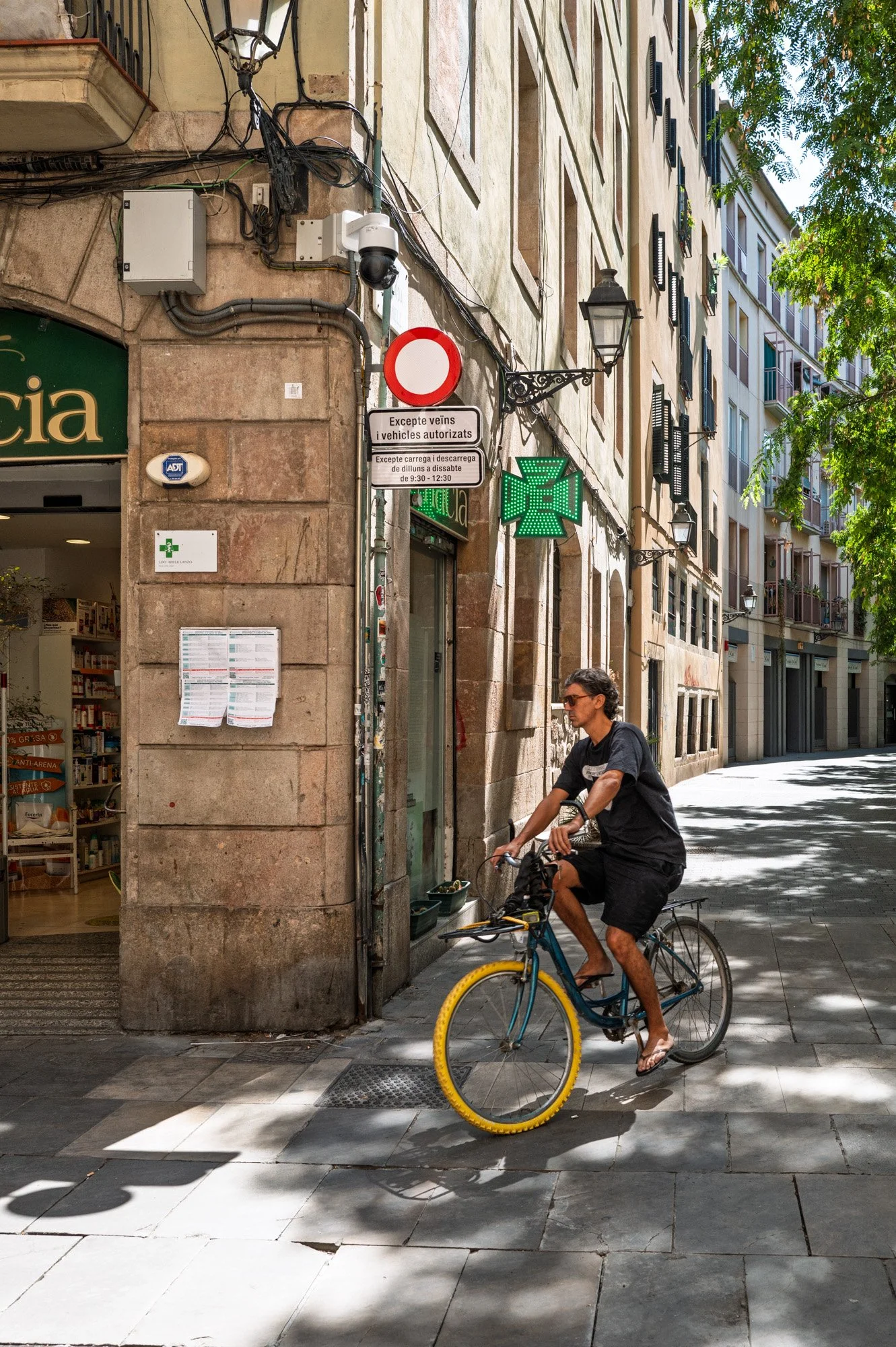 Cyclist passing a pharmacy corner in El Born, Barcelona street photography — Leica Q3