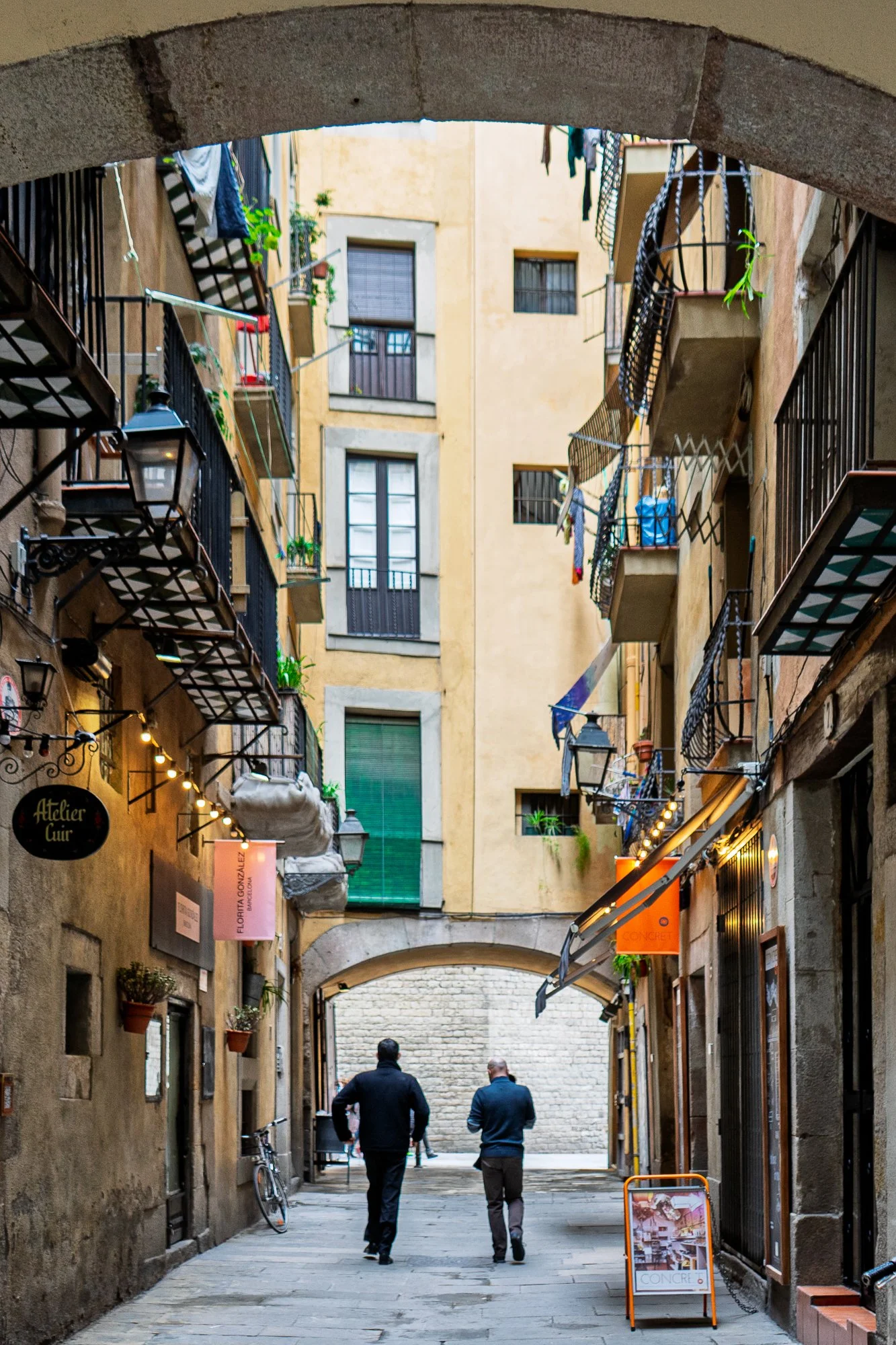 Two men resting in the arcade shade outside Atelier Cuir, El Born — Leica Q3