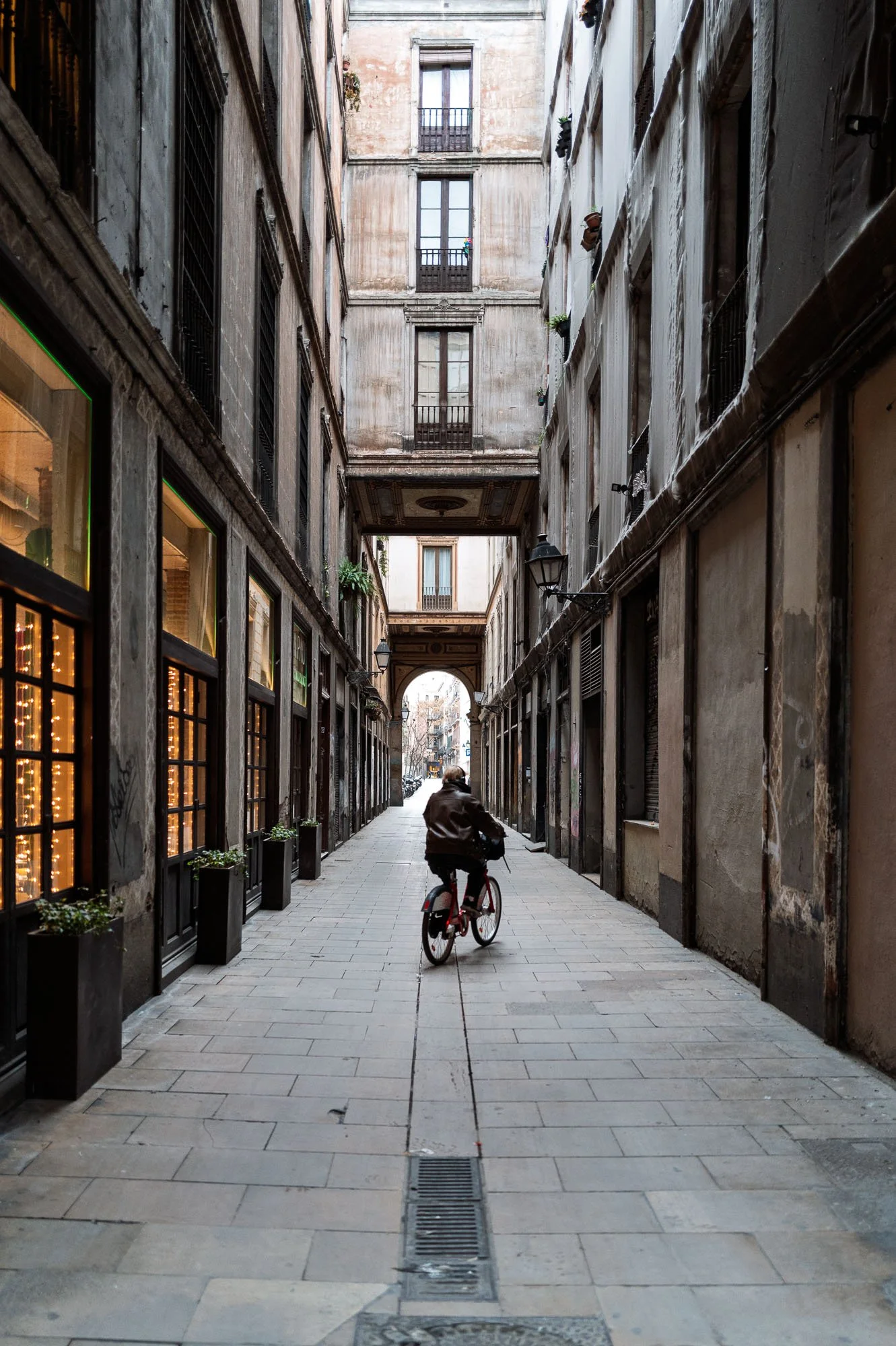 Cyclist in a narrow Barcelona Gothic Quarter alley towards a stone arch, best street photography spot — Leica Q3