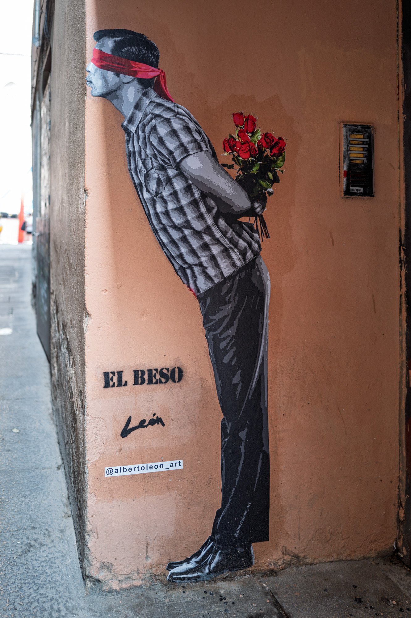El Beso, a street art mural by León in El Born, Barcelona, of a blindfolded man holding roses behind his back