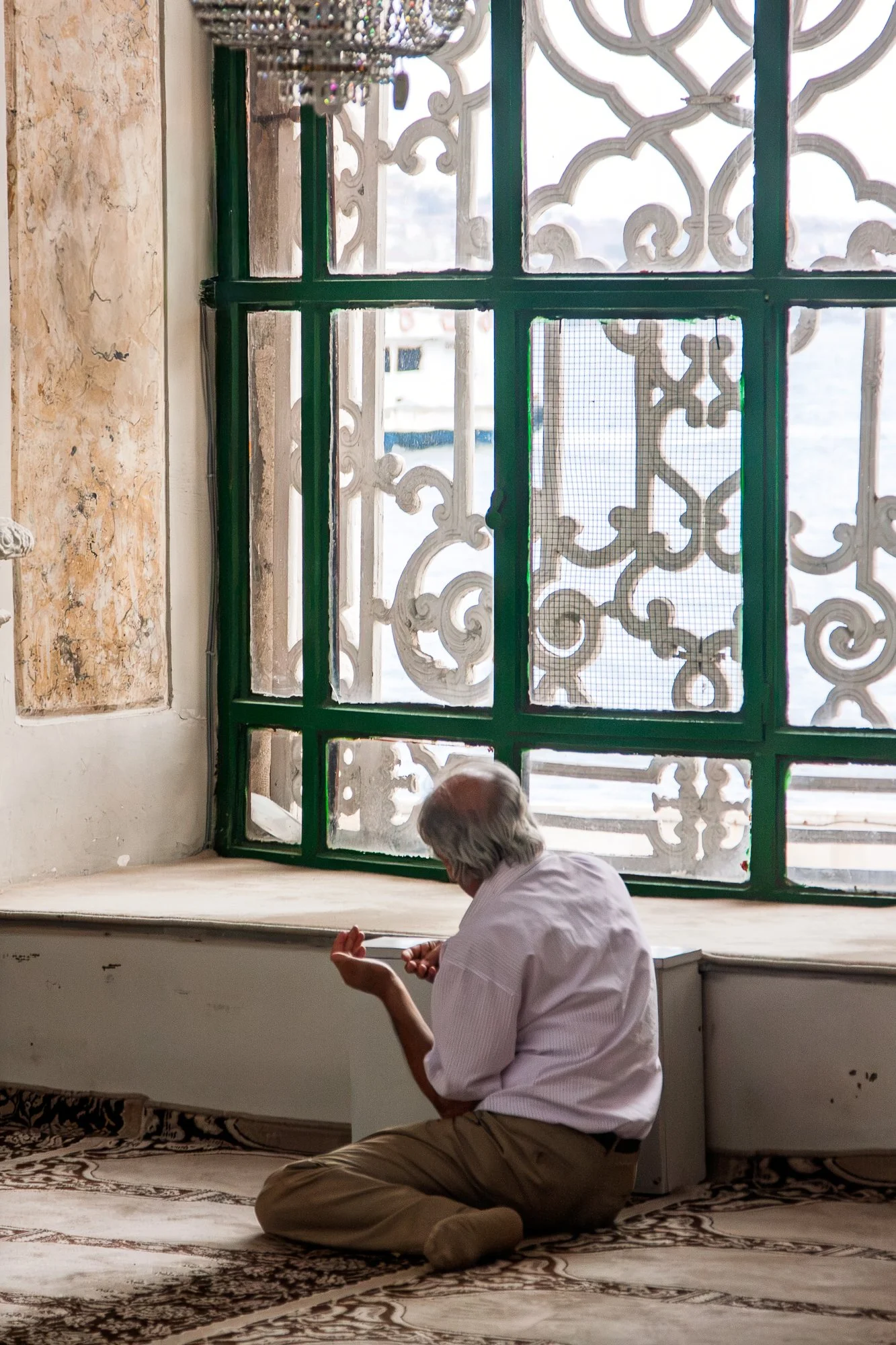 Elderly man praying beside a window overlooking the Bosphorus