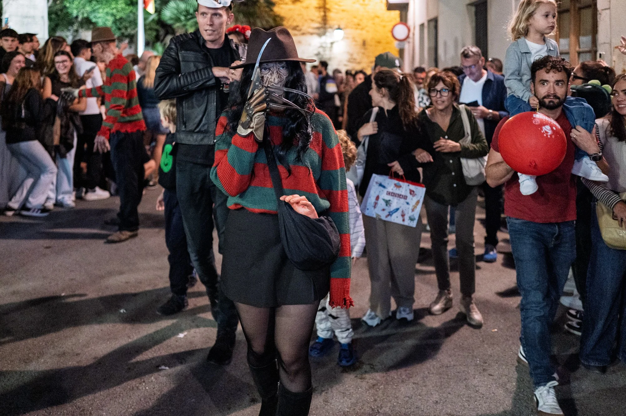 Woman as Freddy Krueger walks past spectators and a child on shoulders with a red balloon, Sitges — Leica Q3
